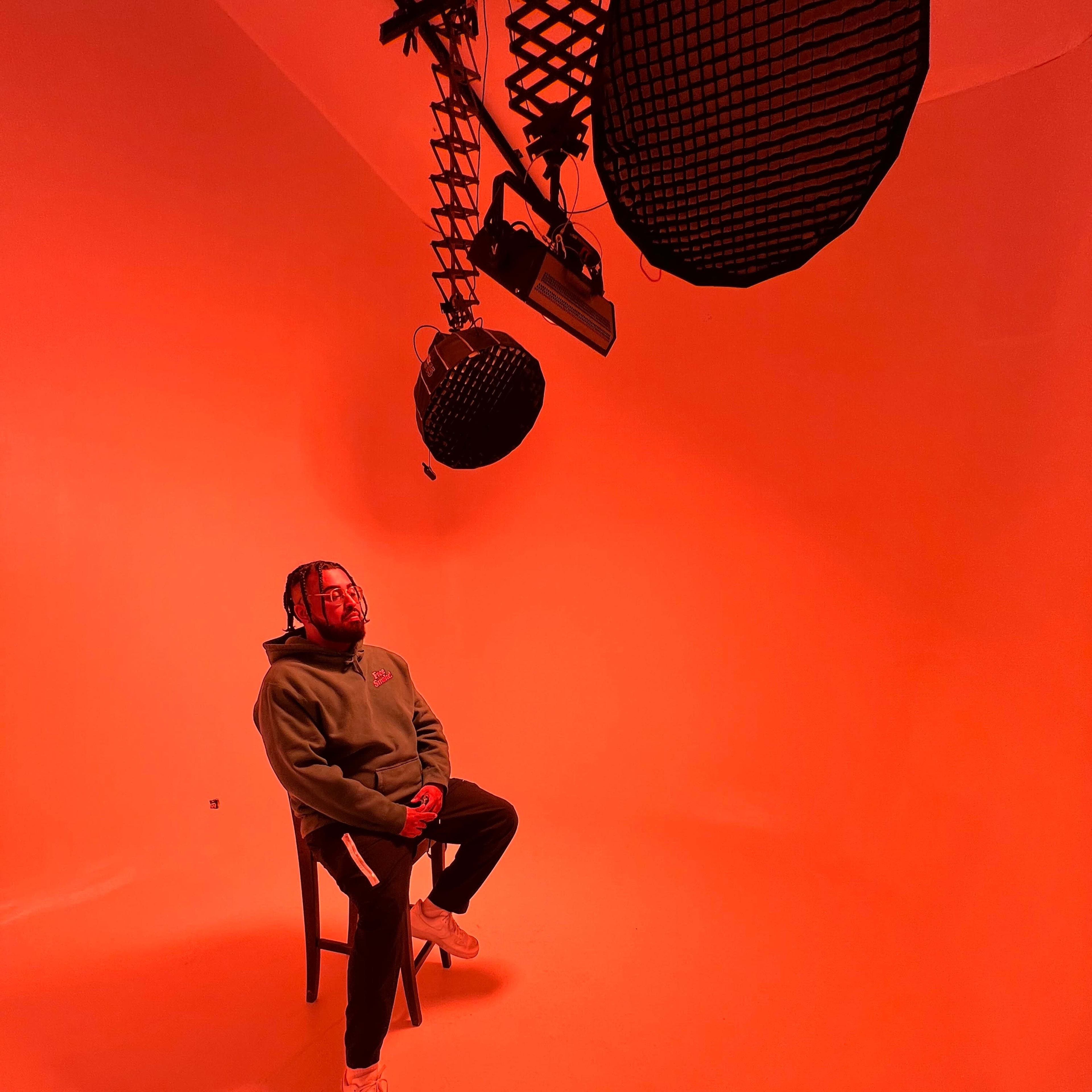 A person sits on a chair in a brightly lit orange studio with overhead lighting fixtures.