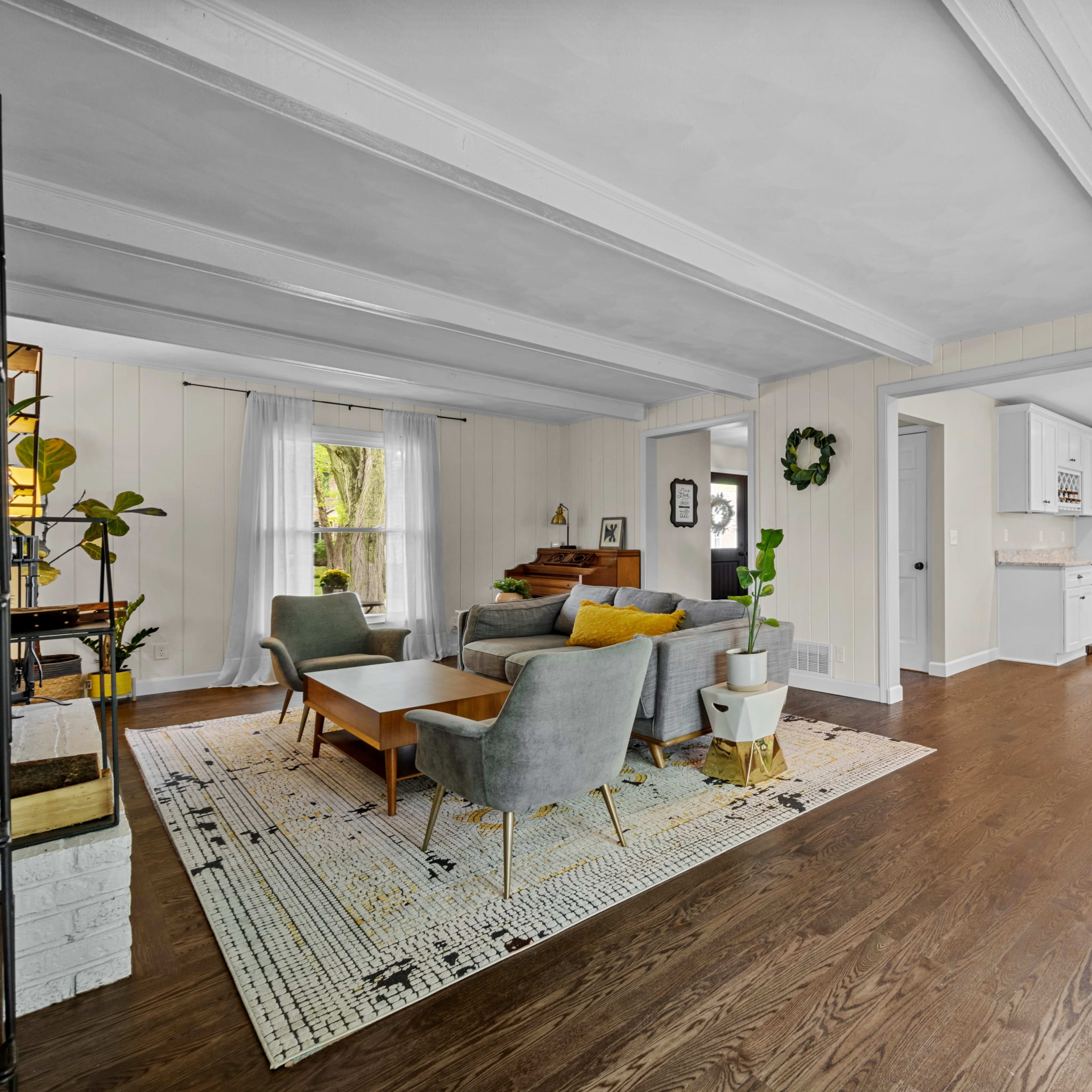 A modern living room with gray and wooden furniture, separated from a kitchen area by an archway.
