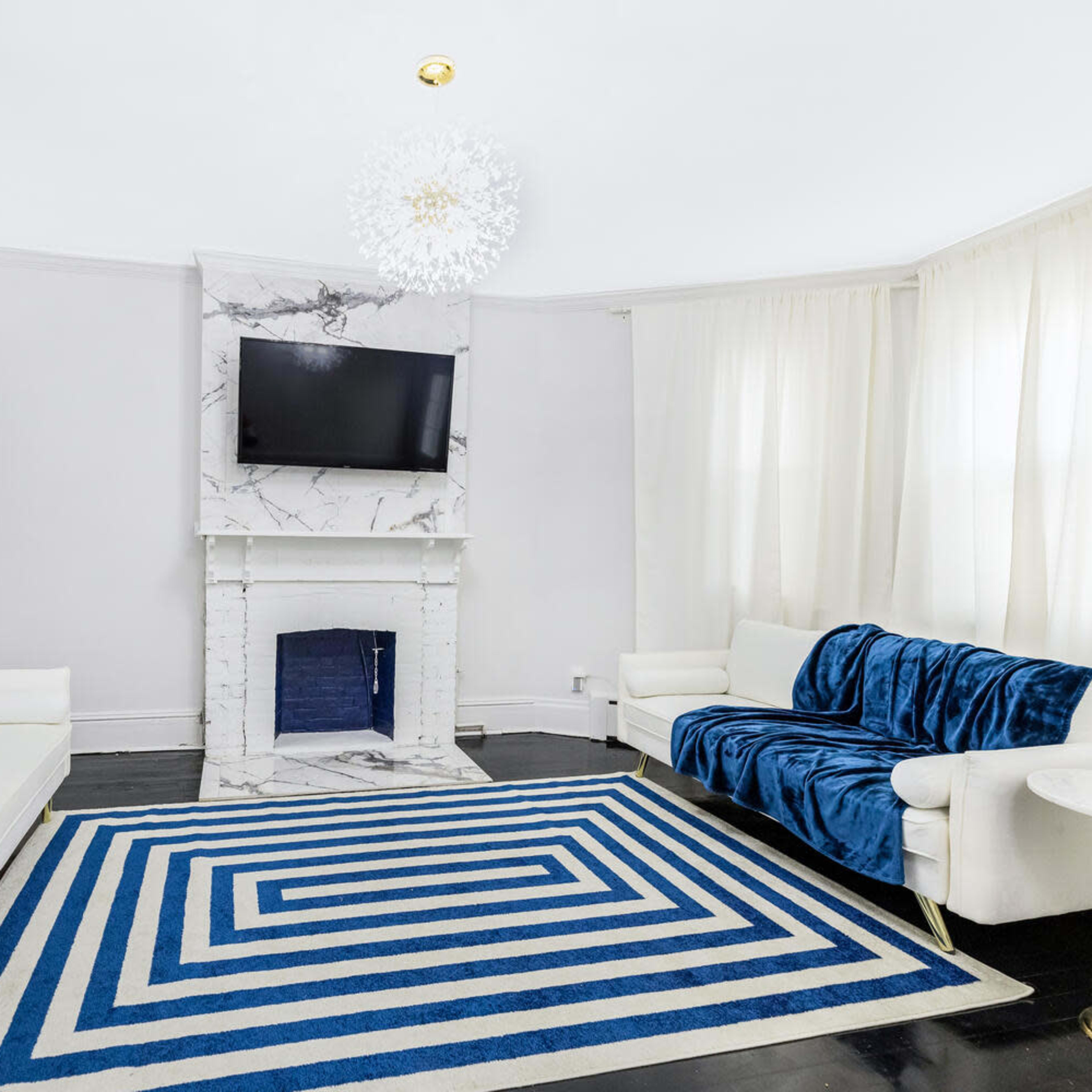 The scene depicts a modern living room featuring a marble fireplace, a wall-mounted television, two sofas, and a striped area rug.