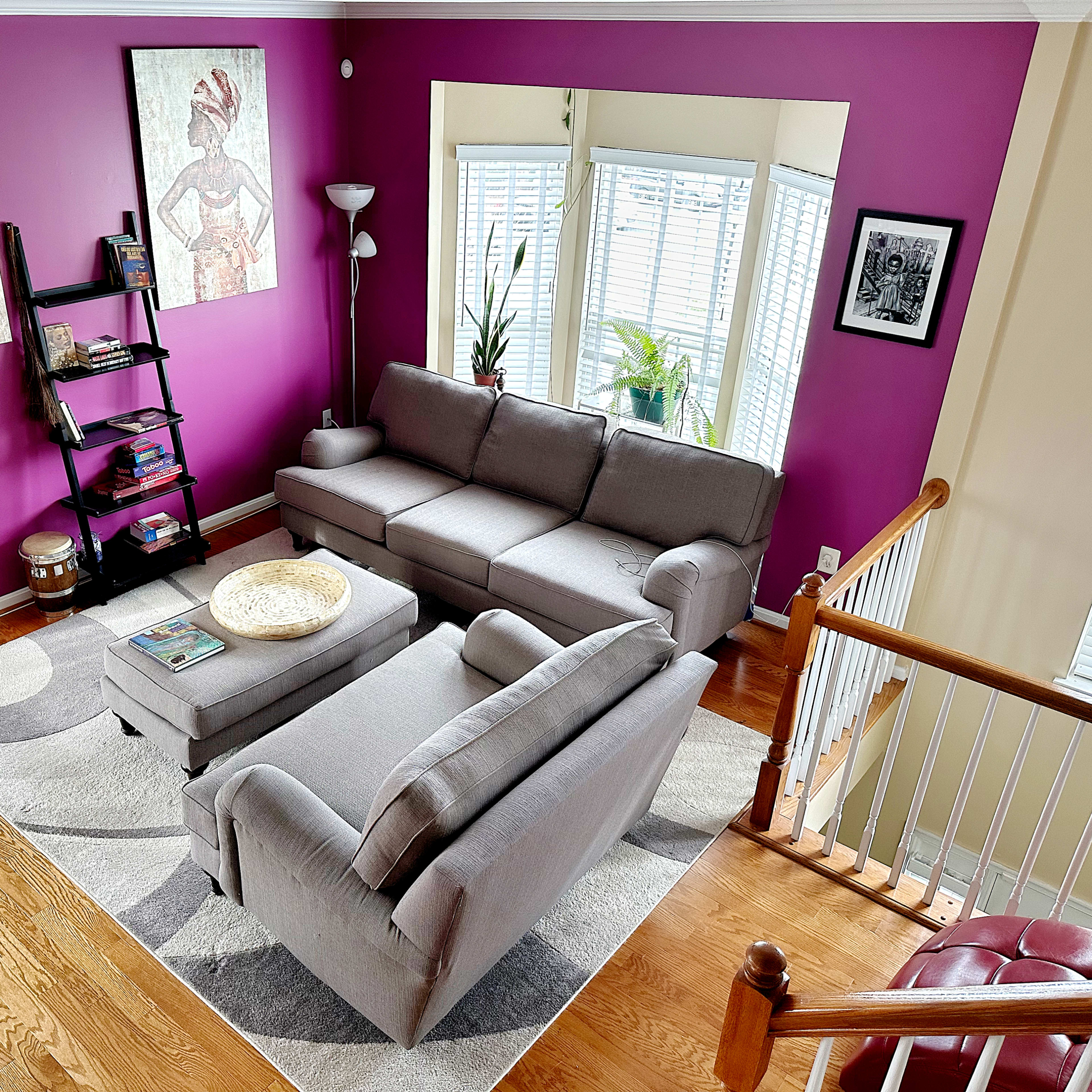 A living room with a gray sectional sofa, a coffee table, a patterned rug, and purple walls adorned with two large framed artworks.
