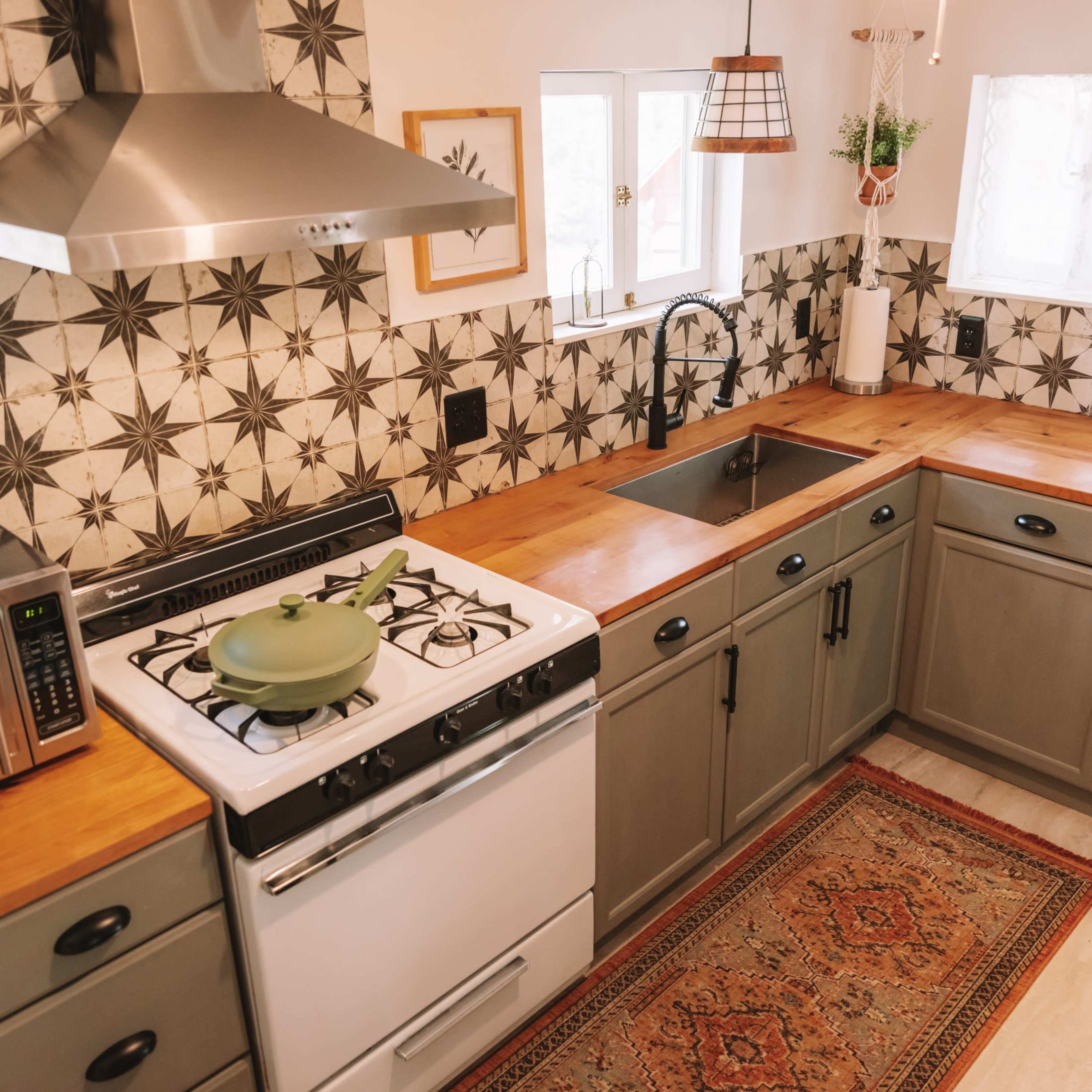 A modern kitchen with a gas stove, a stainless steel hood, wooden countertops, and patterned tiles on the walls.