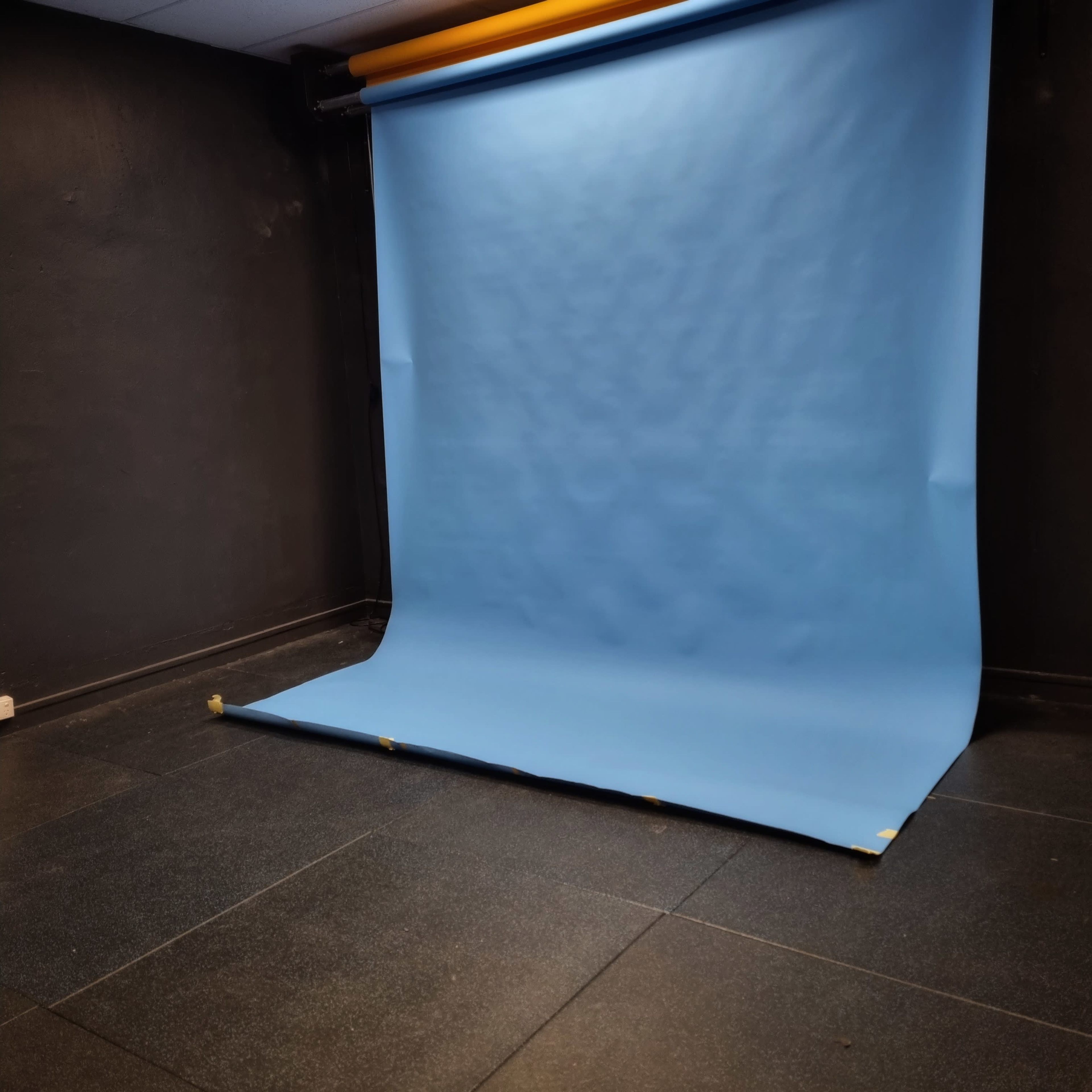 An empty studio space with a blue backdrop and dark tiled flooring.