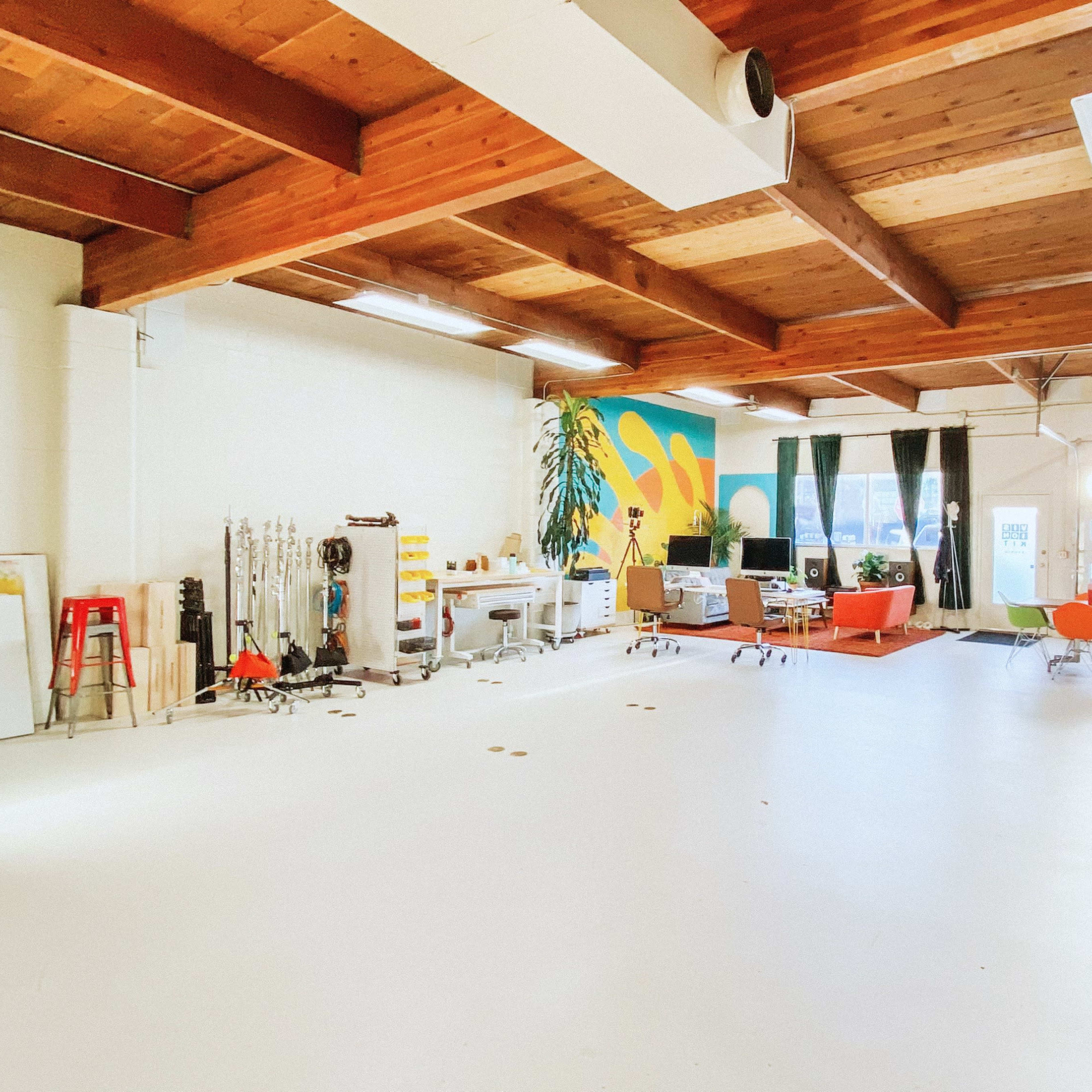 A spacious, well-lit studio with wooden beams, colorful walls, and various furniture arrangements, including seating areas and workspaces.