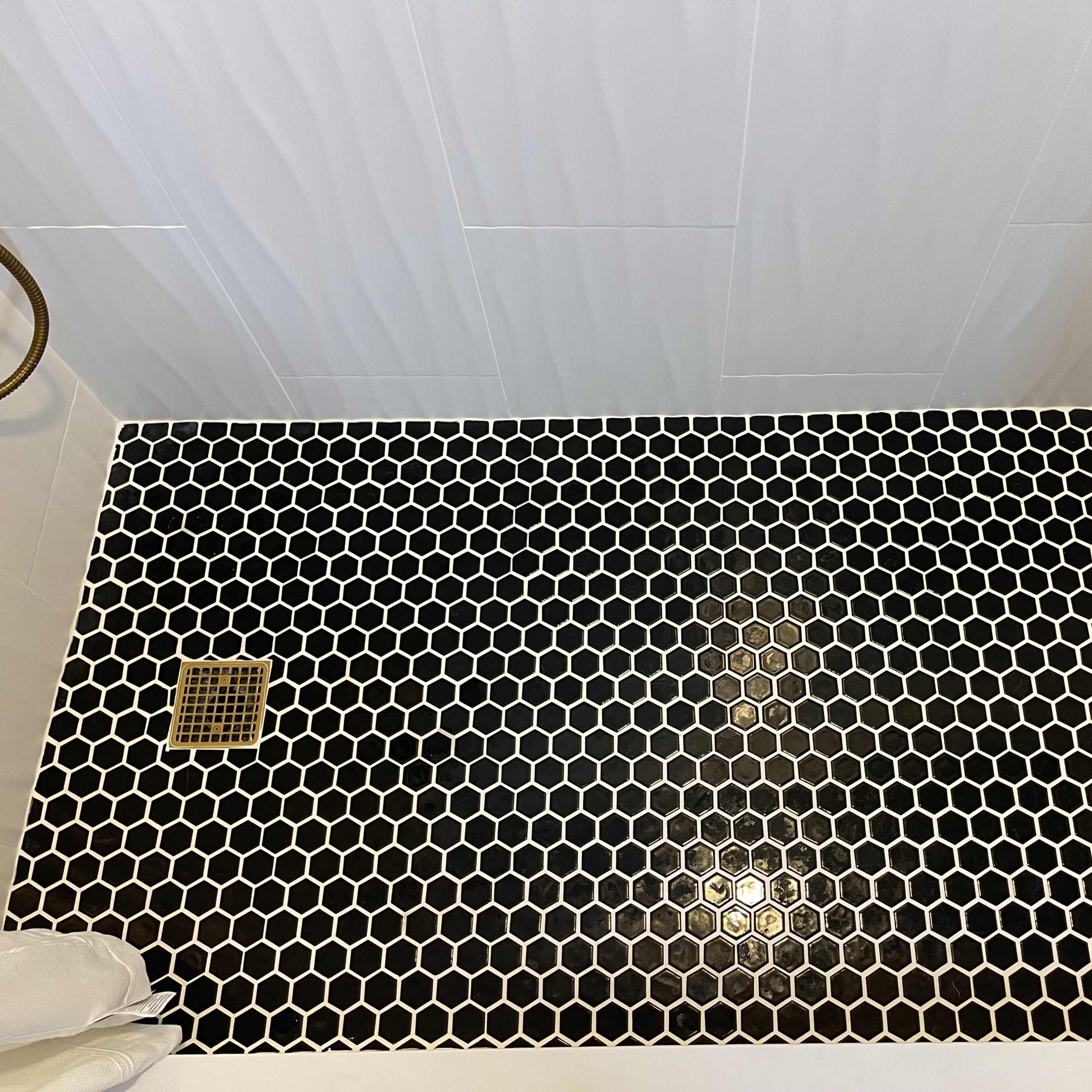 A shower floor covered with black and white hexagonal tiles and a metal drain in the corner.