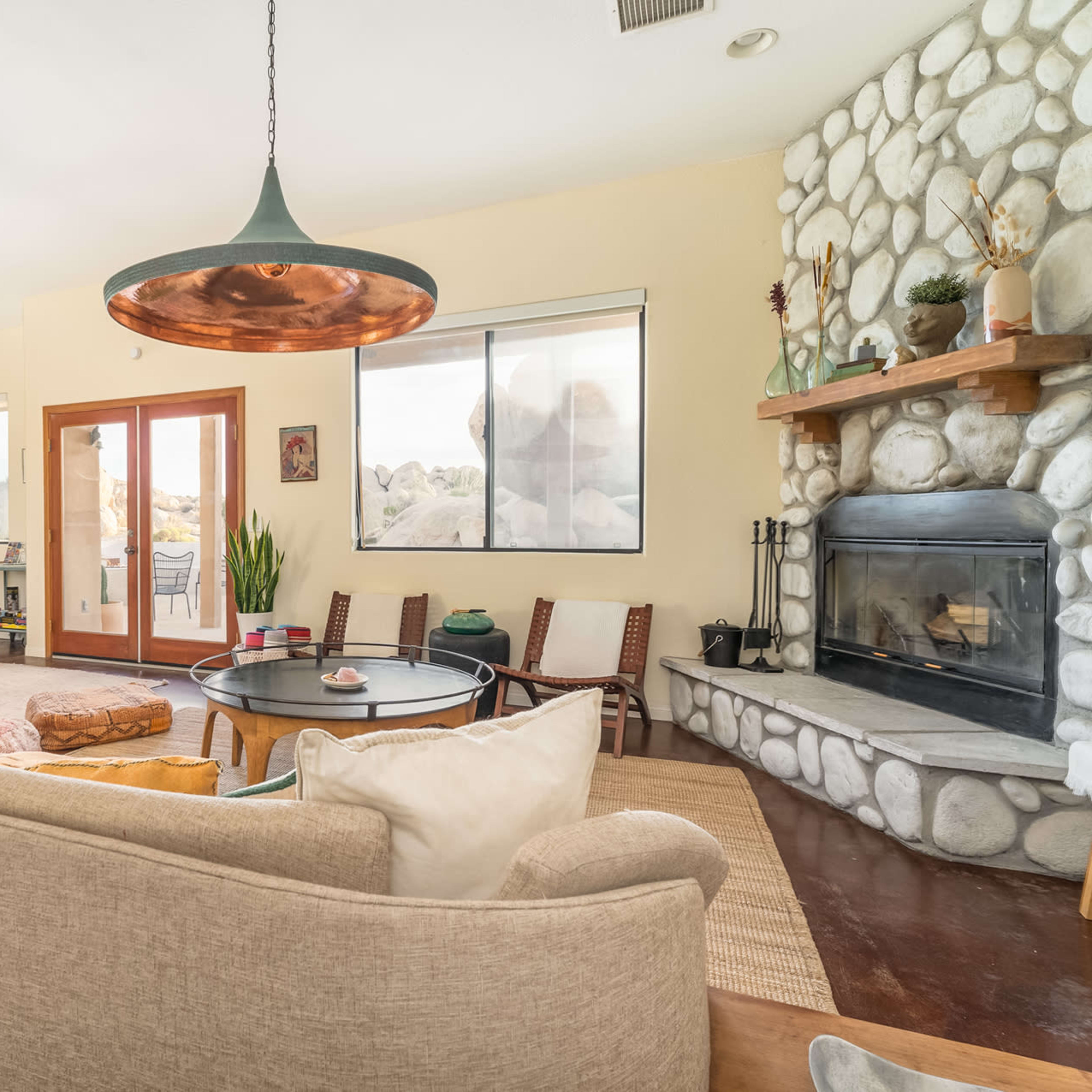A modern living room with a stone fireplace, large windows, and a dining area featuring a wooden table and chairs.