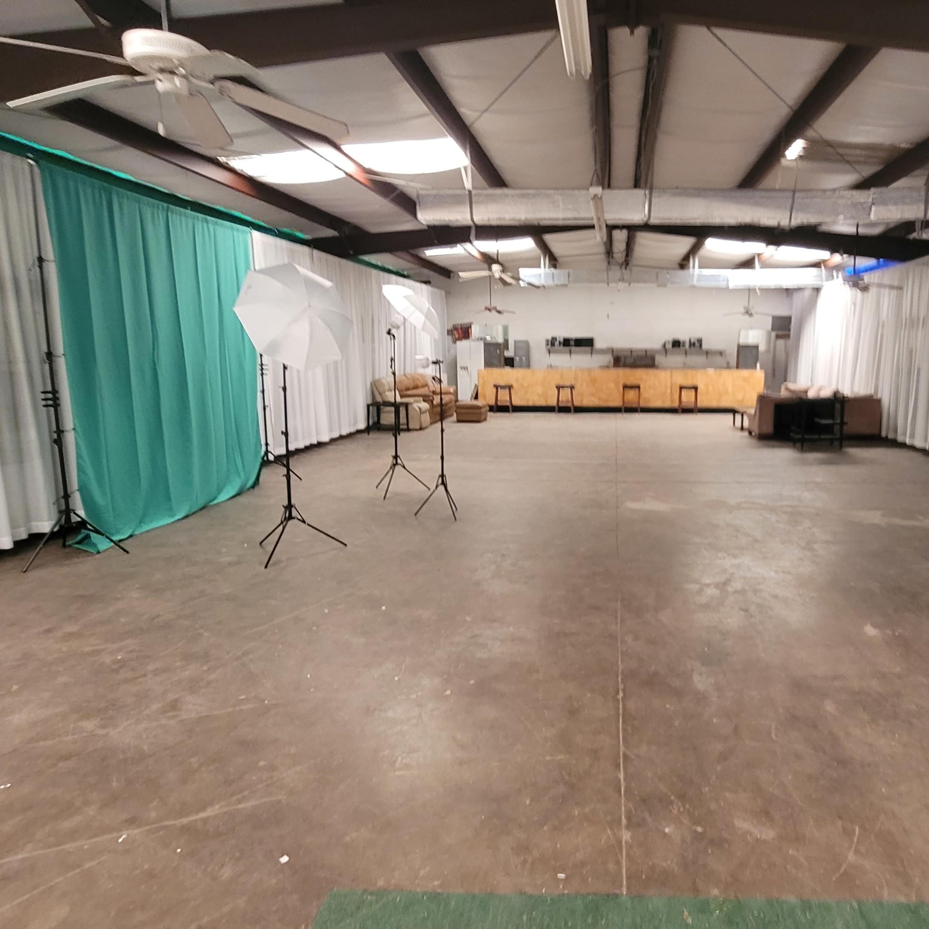 A spacious indoor area with a concrete floor, draped fabric in teal and white, and photography equipment set up.