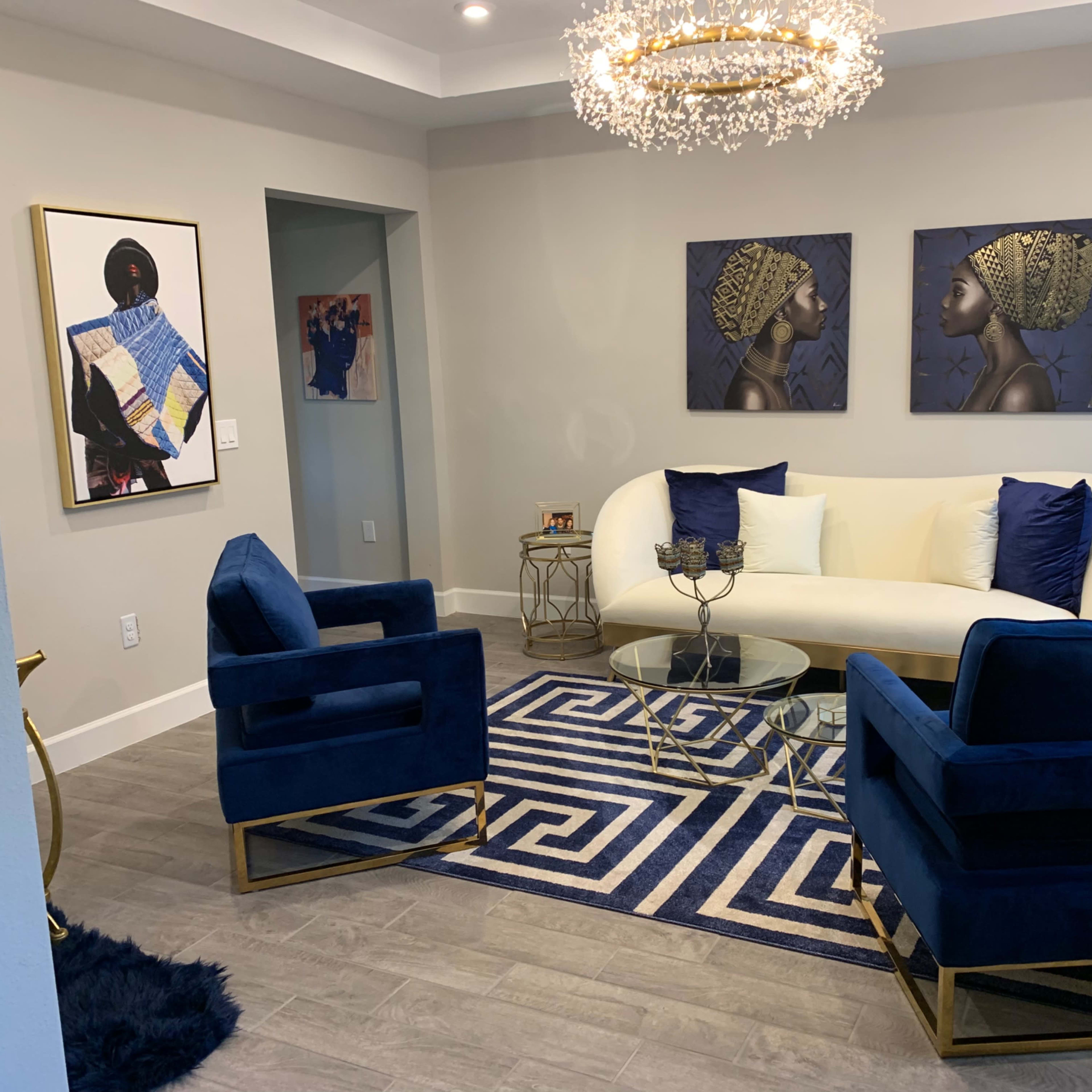 A modern living room with a white sofa, two blue chairs, a glass coffee table, and artwork on the walls.