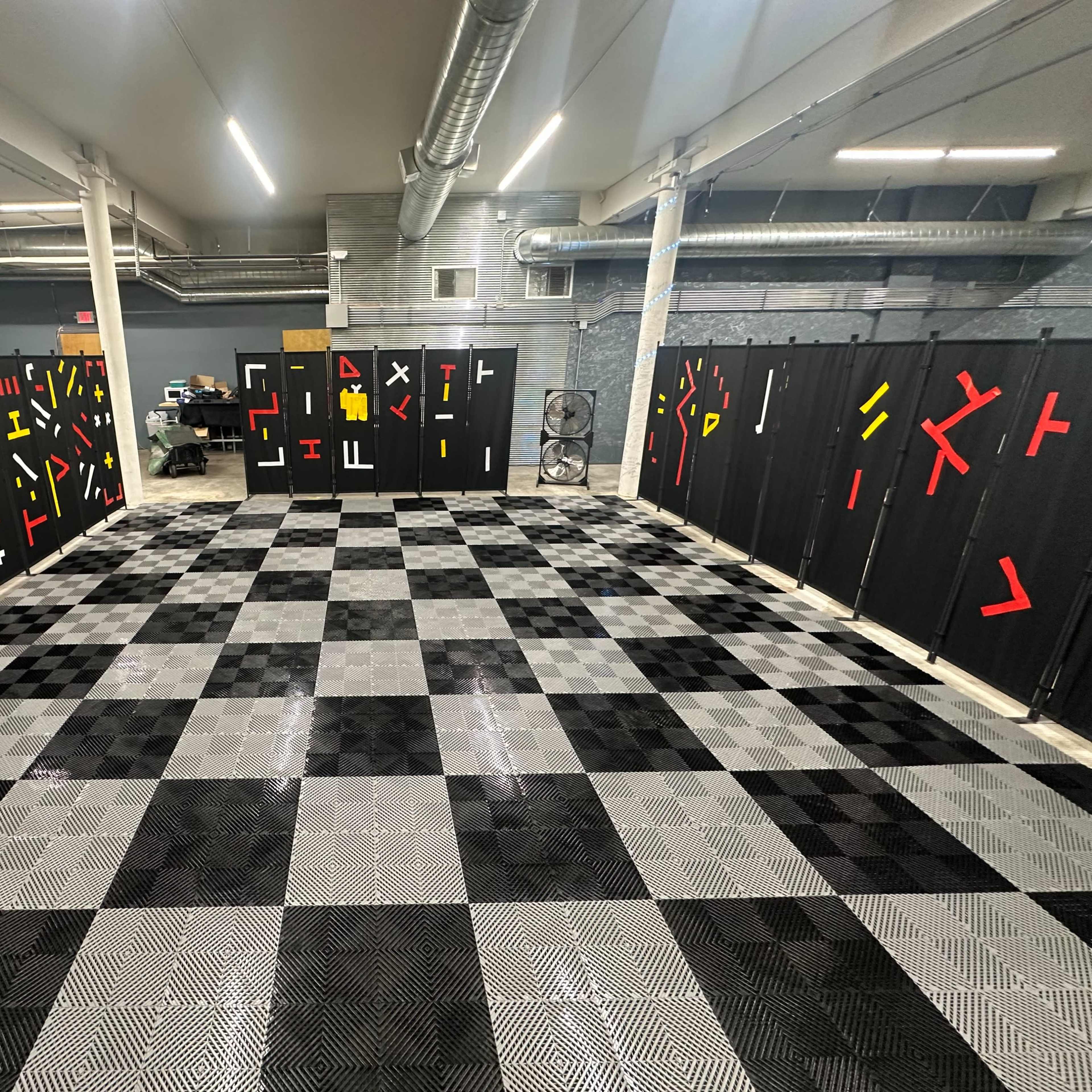 A large room with a checkered black and gray floor, surrounded by black panels adorned with red, yellow, and white geometric shapes.