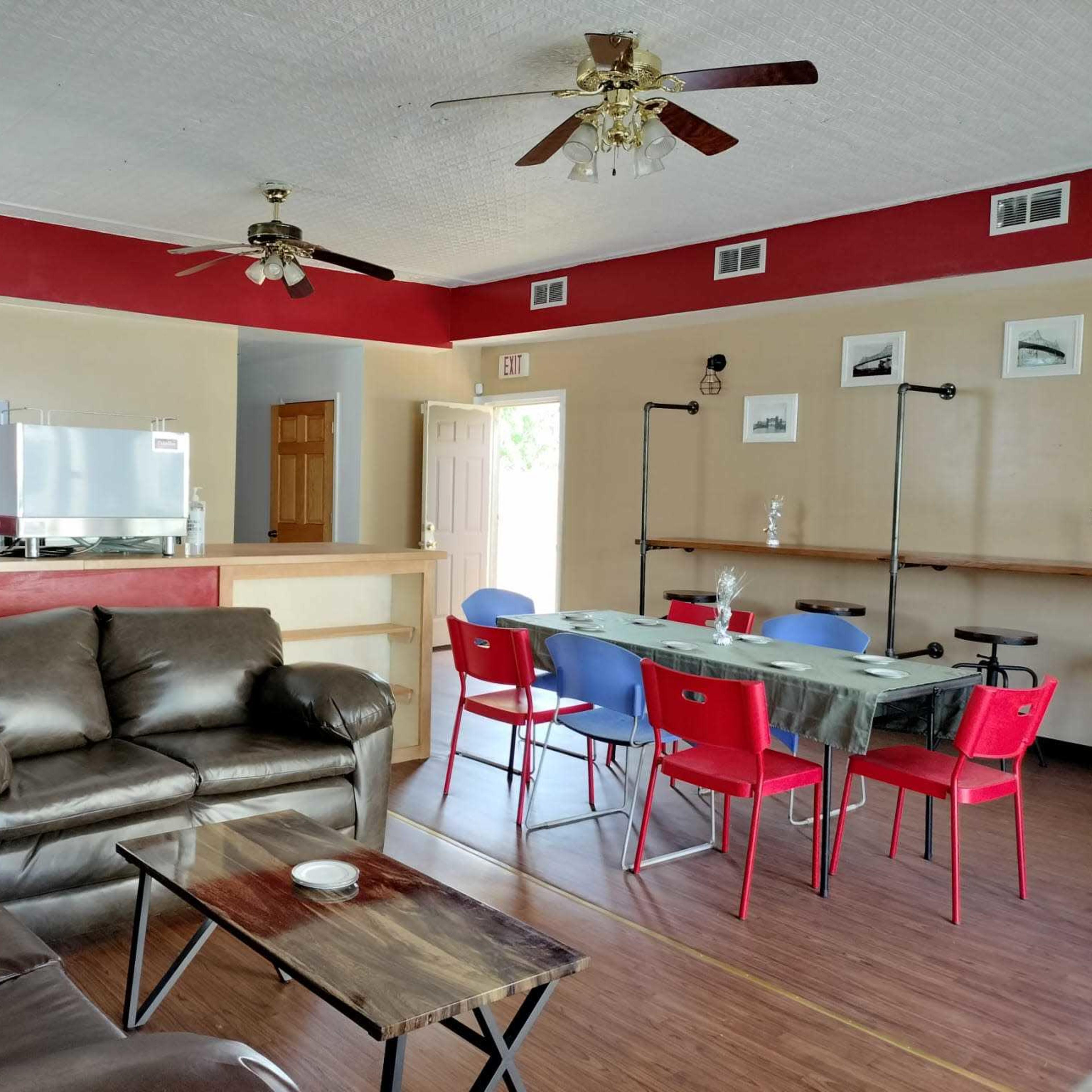 A living area with a brown leather couch, a wooden coffee table, a dining table with red chairs, and a kitchen area in the background.