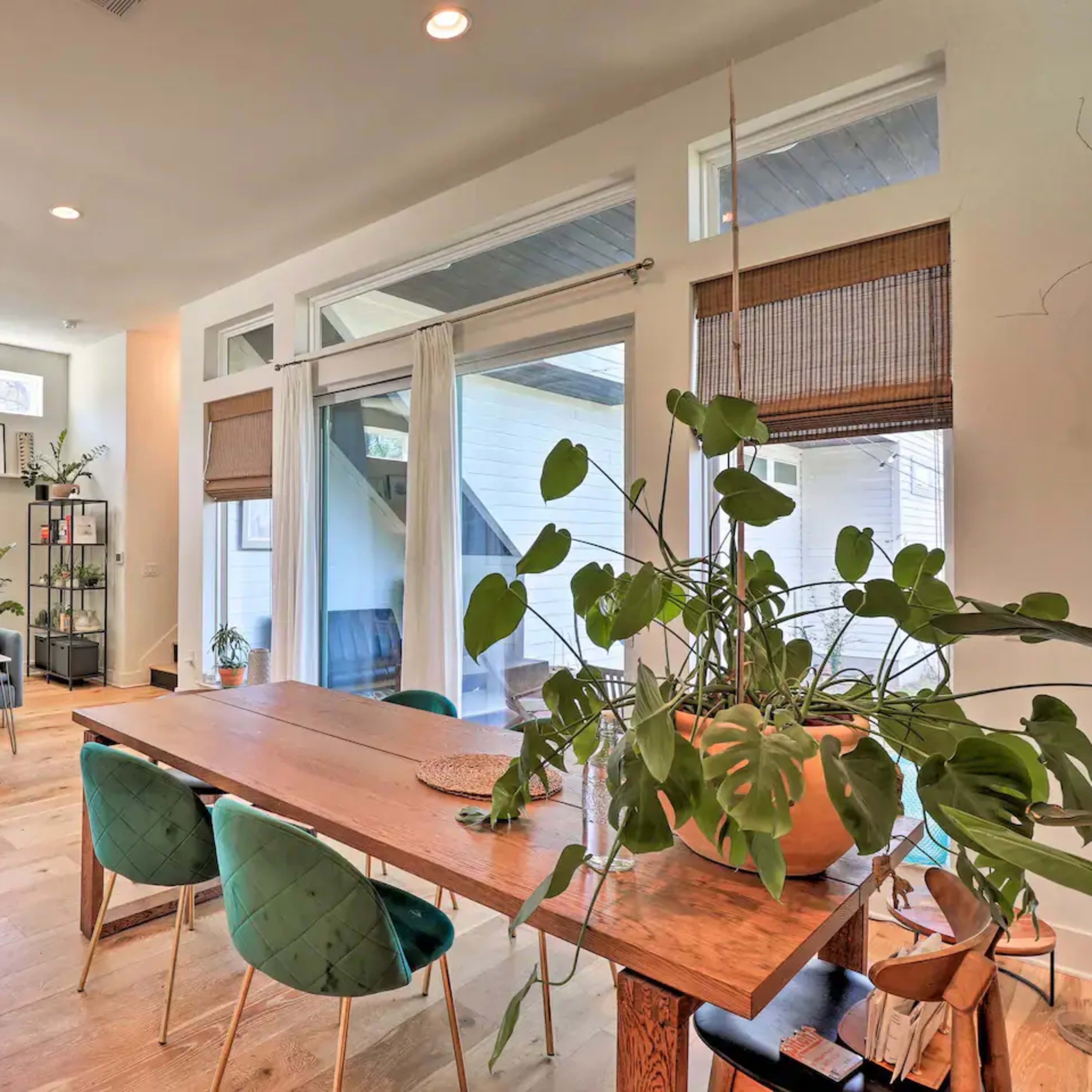 A modern living space featuring a dining table with green chairs, potted plants, and a lounge area with a sofa.