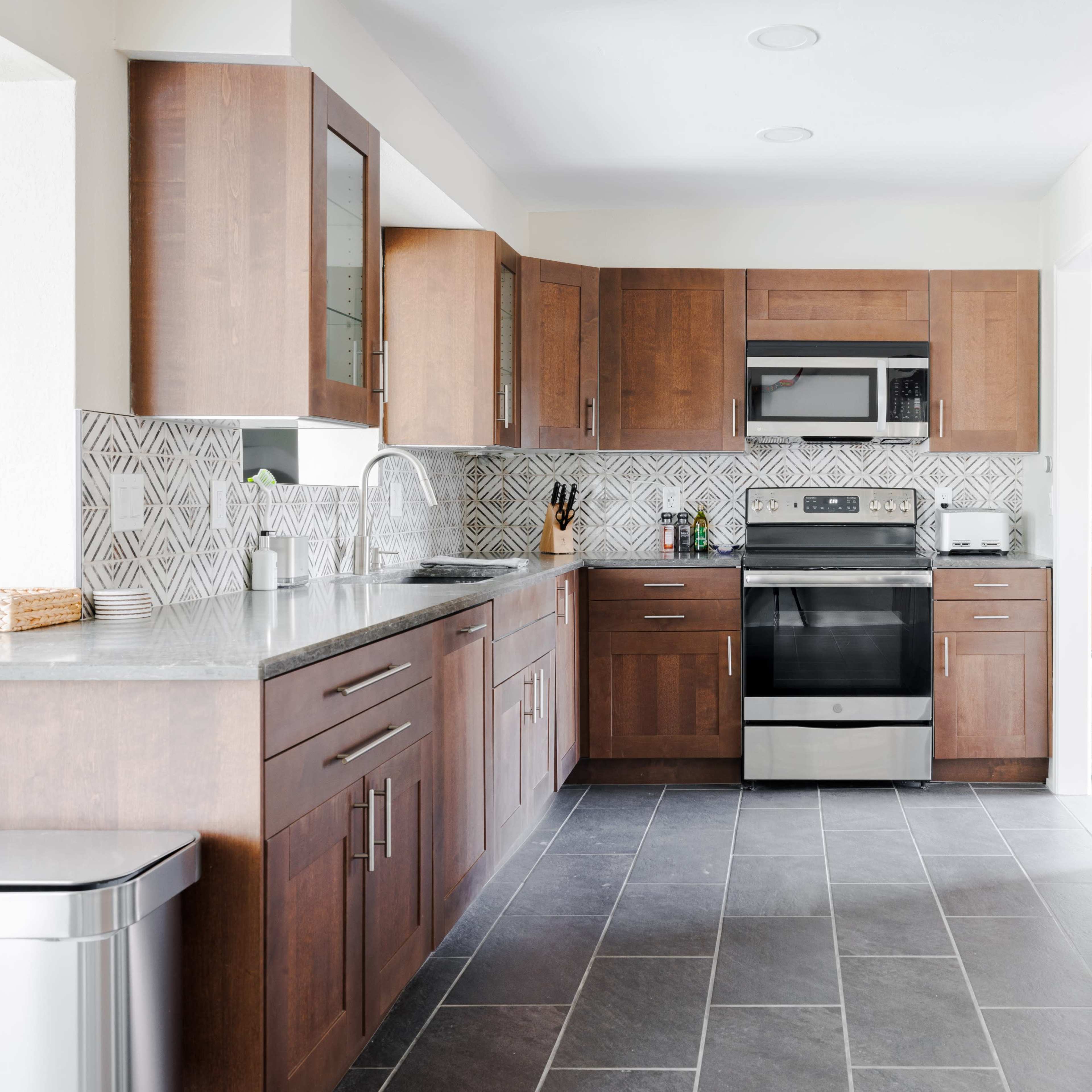 A modern kitchen featuring wooden cabinets, a stainless steel refrigerator, and a black tile floor.