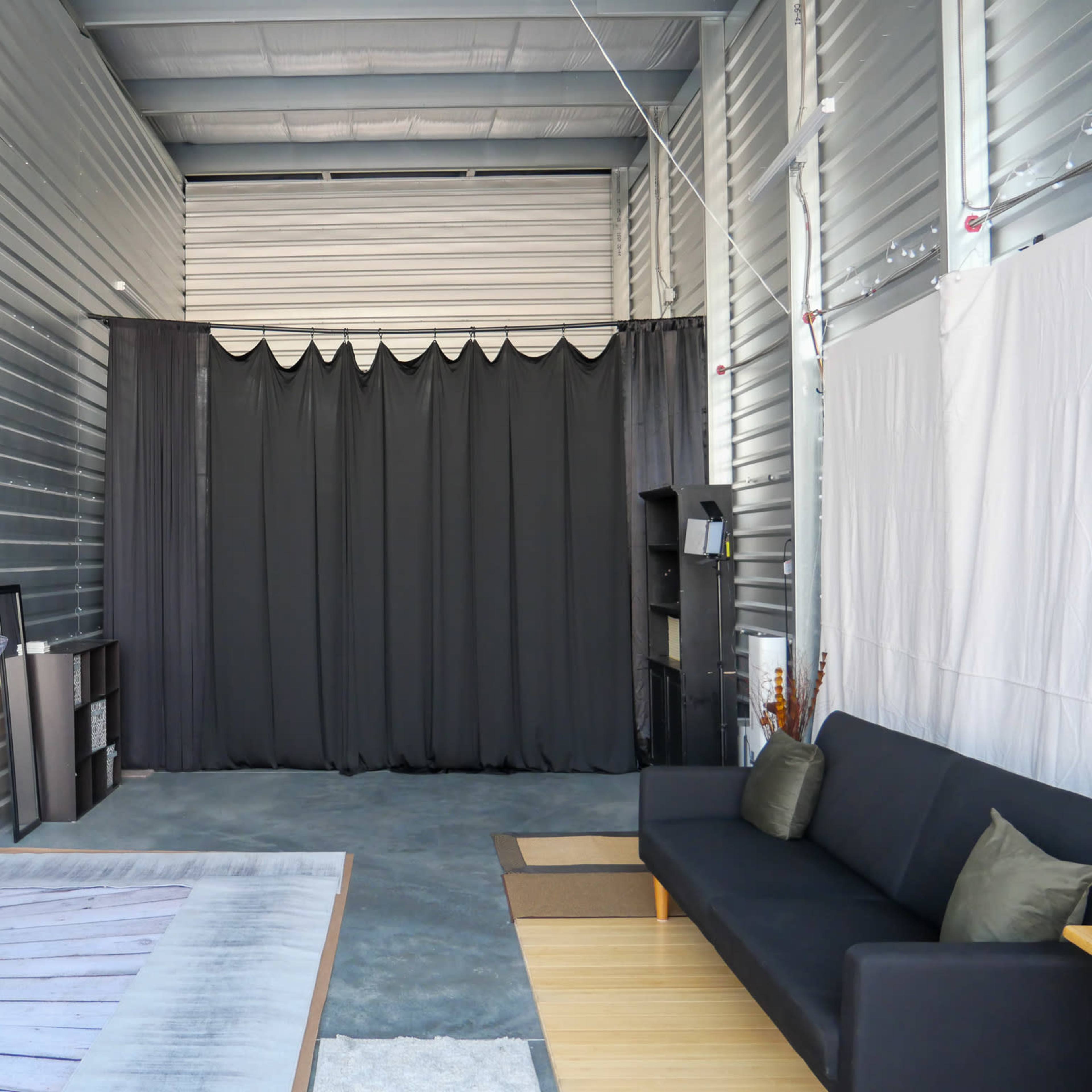 A spacious studio with gray metal walls, featuring a black curtain backdrop and a wooden floor area, along with a black sofa and minimalist decor.