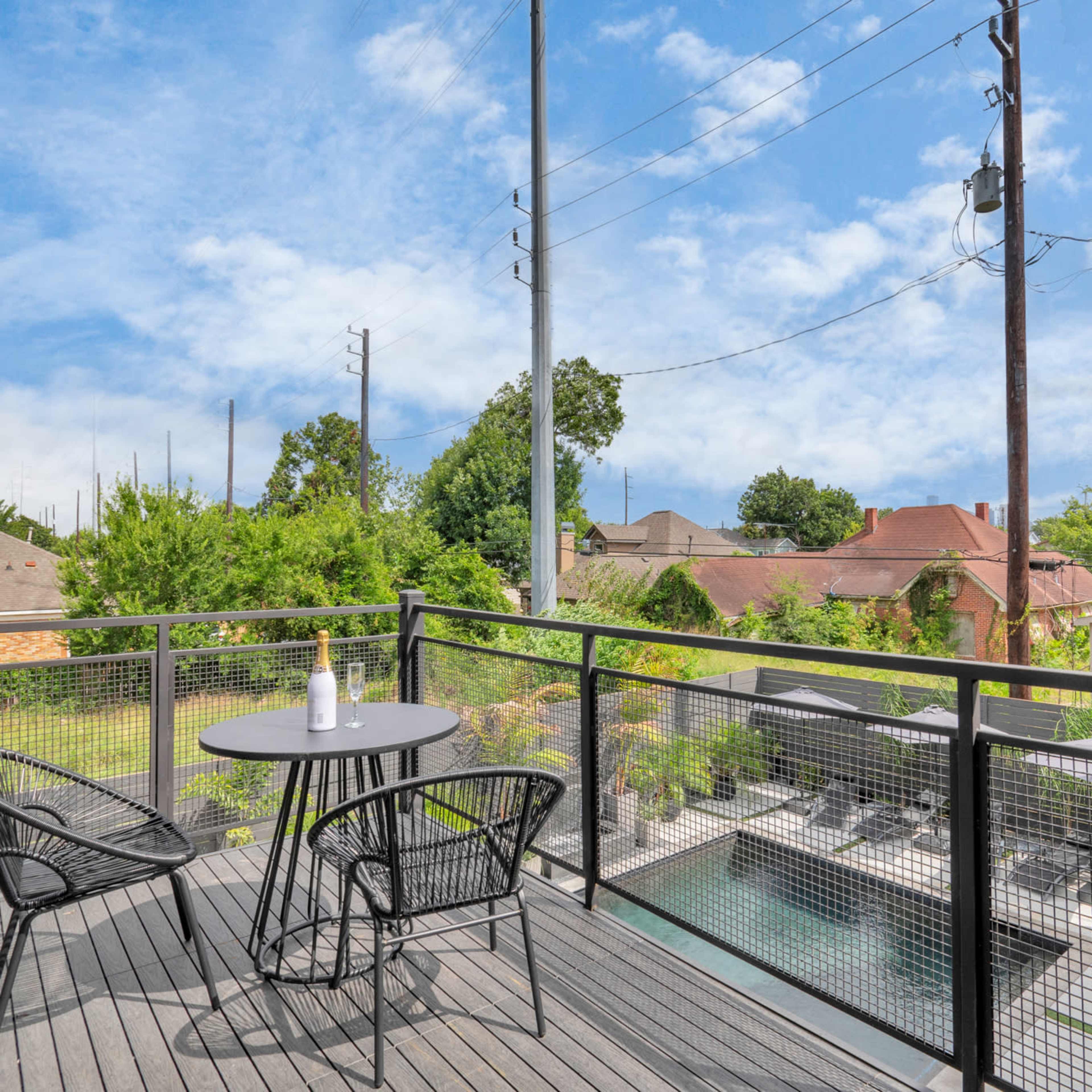 A balcony features two black chairs and a small table overlooking a pool and surrounding greenery.