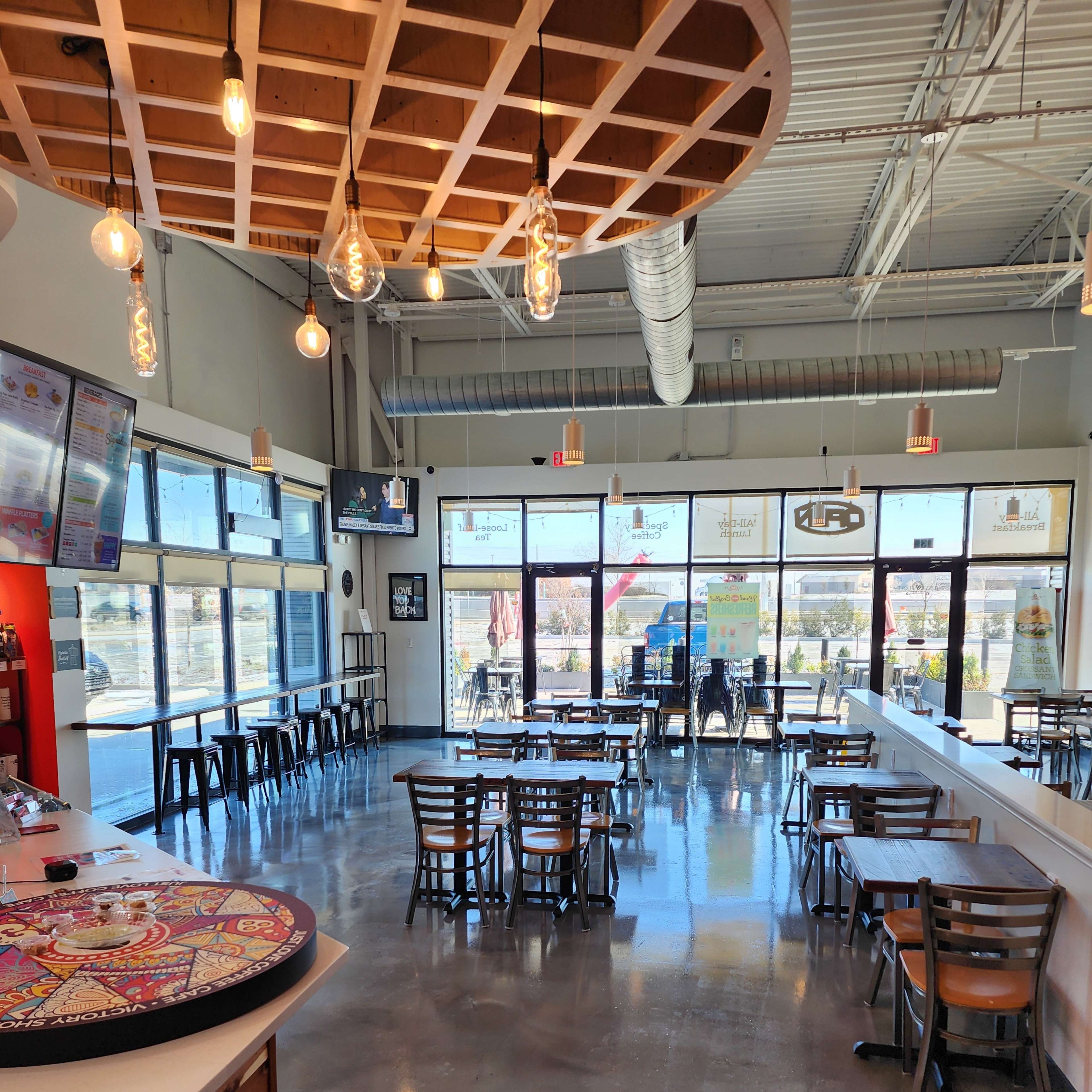 A modern dining space with large windows, polished concrete floors, and a mix of tables and chairs arranged for customers.