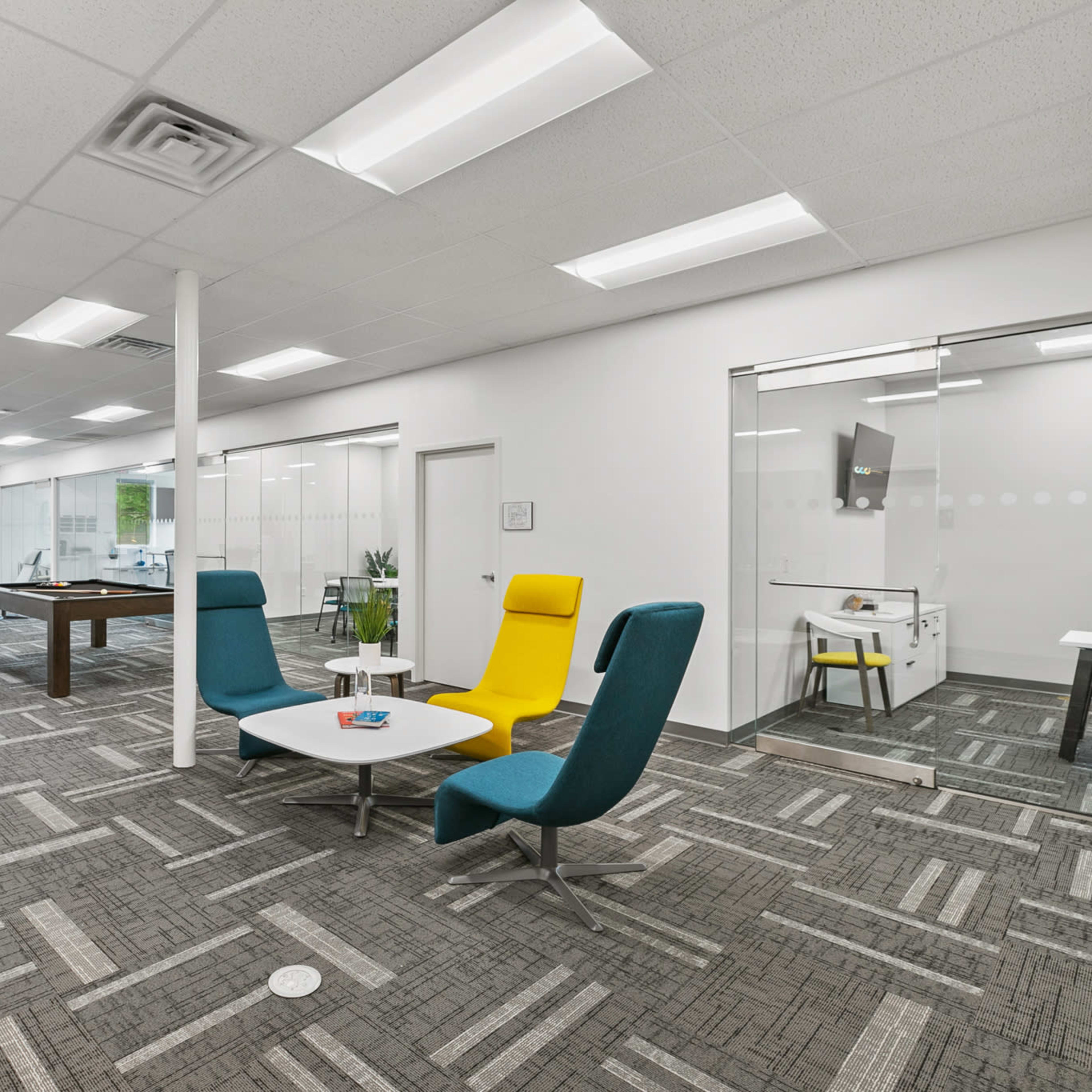 A modern office space with a pool table, bright seating areas, and glass-walled meeting rooms.