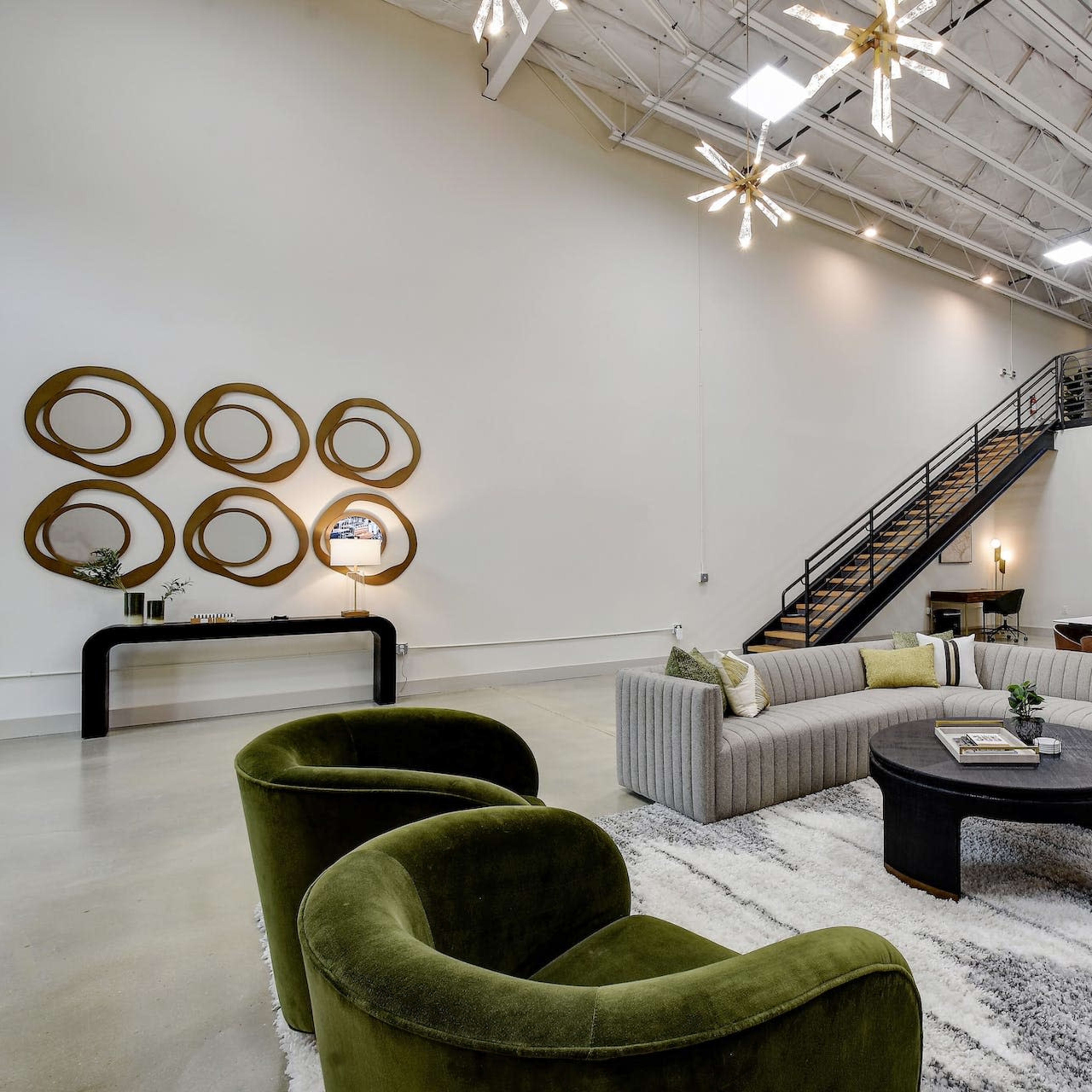 A spacious modern living area with a large sectional sofa, a round coffee table, and a staircase leading to a lofted area.