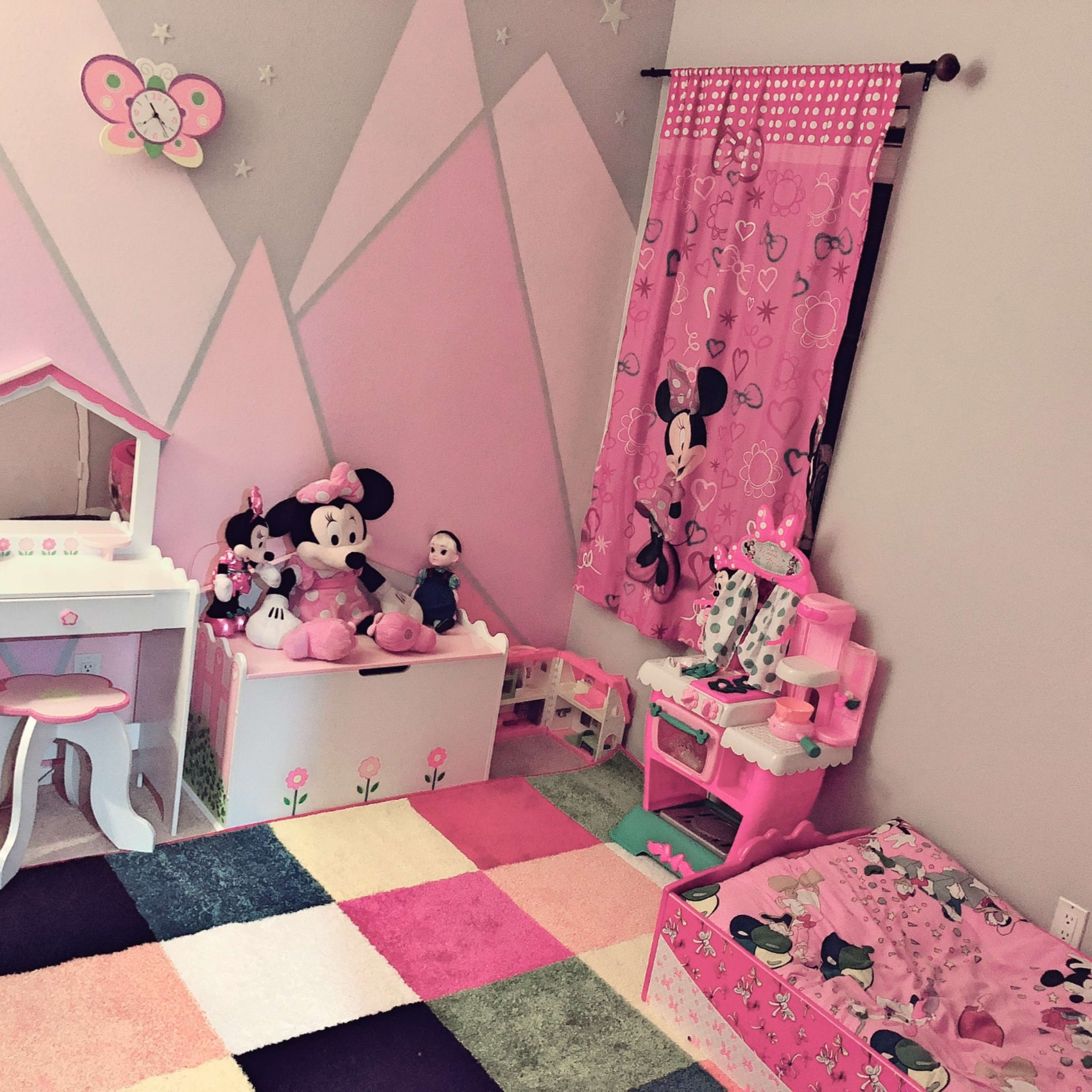 A children's bedroom decorated in pink with a variety of Minnie Mouse-themed items, including a bed, a vanity, and stuffed toys.