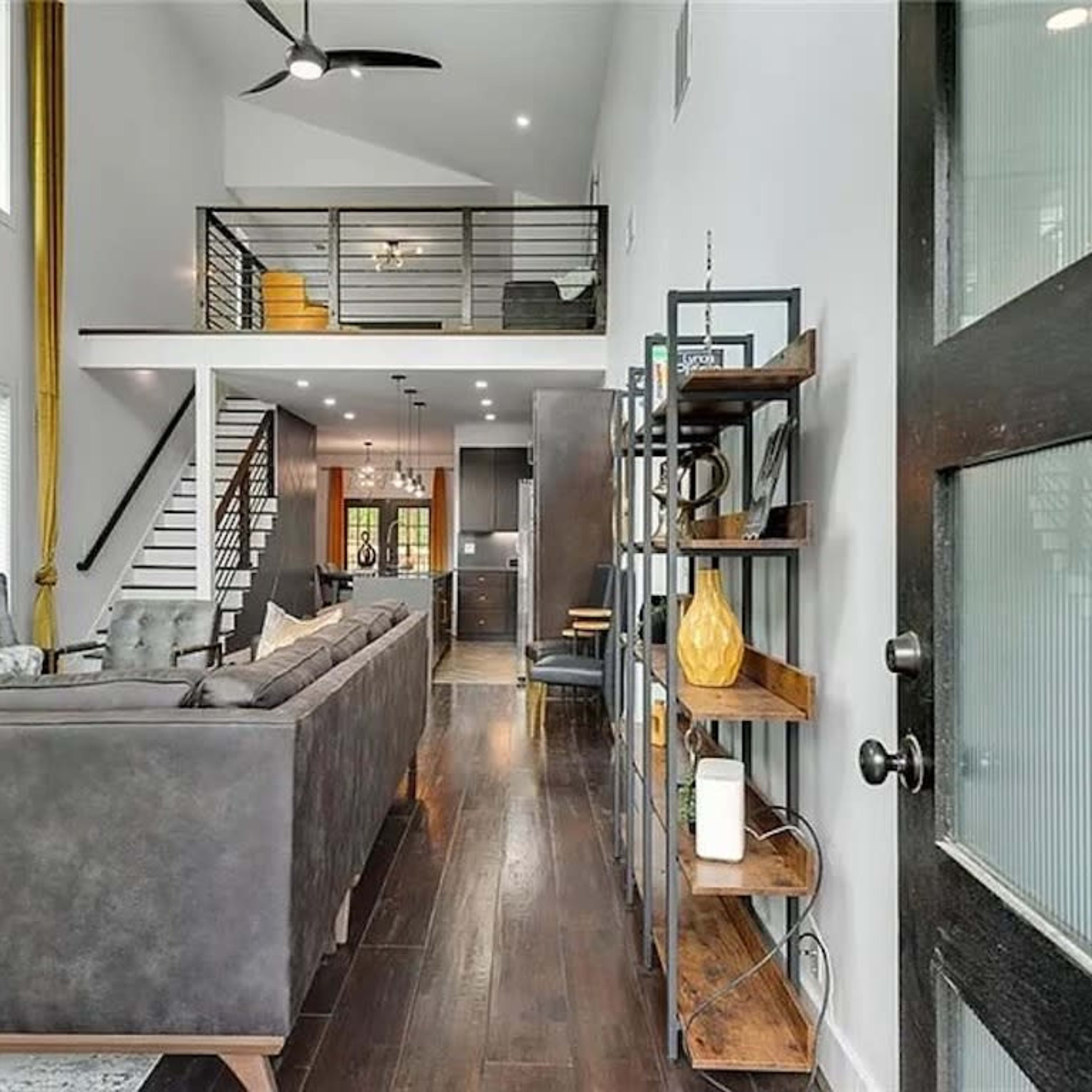 A modern living room with a large sectional sofa, a staircase leading to a second level, and an open layout that connects to a kitchen area.