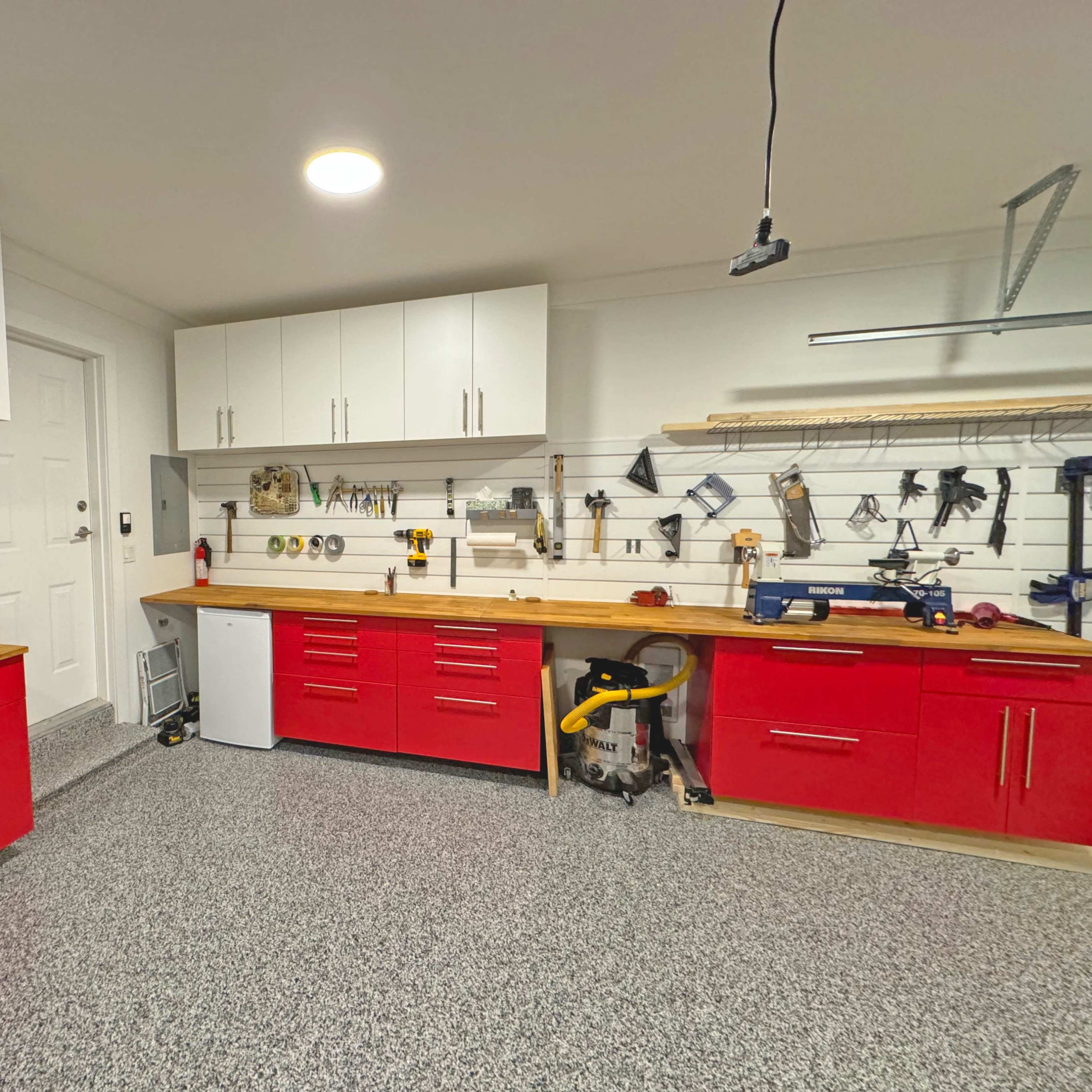 A well-organized garage workspace with red cabinets, a wooden countertop, and various tools displayed along a wall.