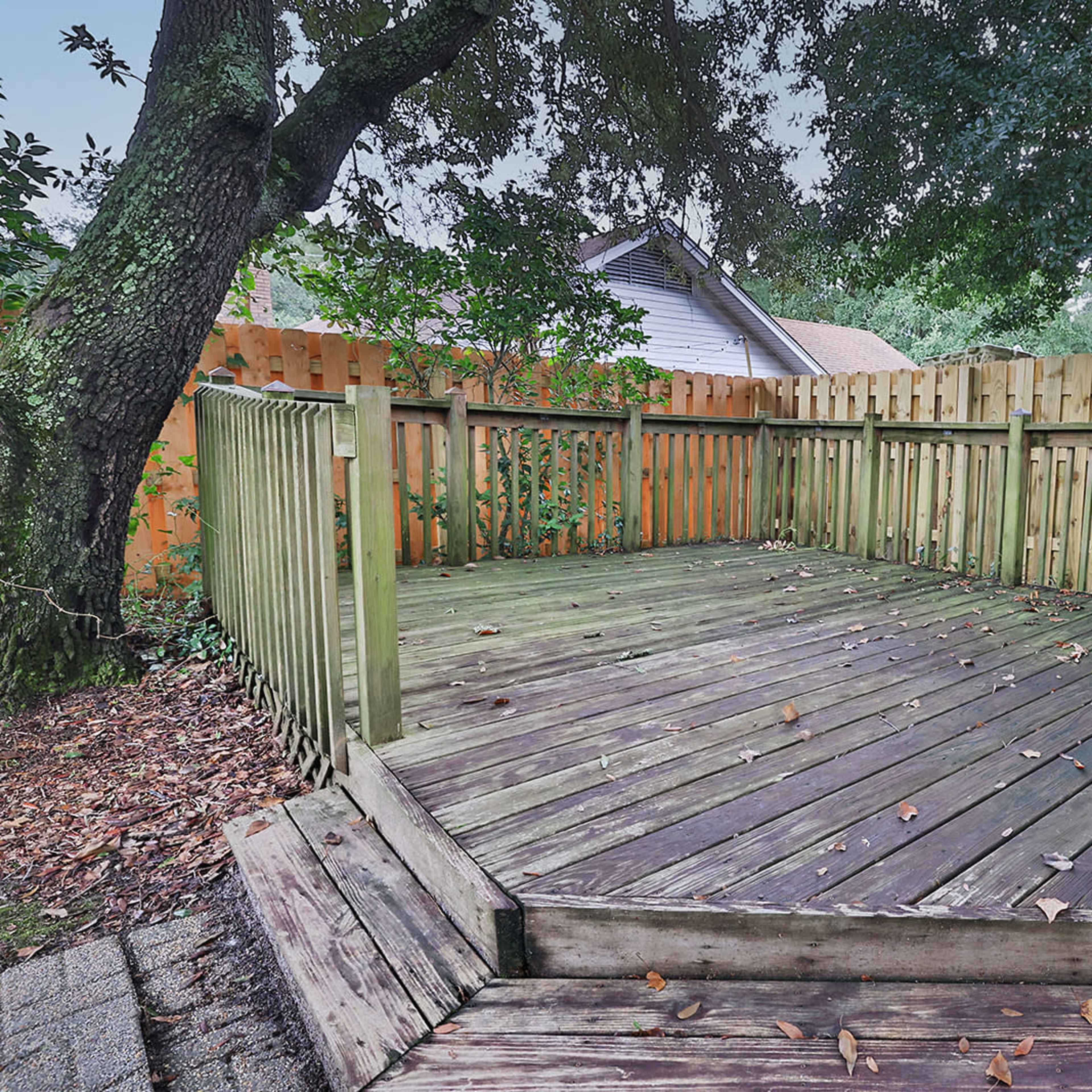 A wooden deck surrounded by a wooden fence and two trees.