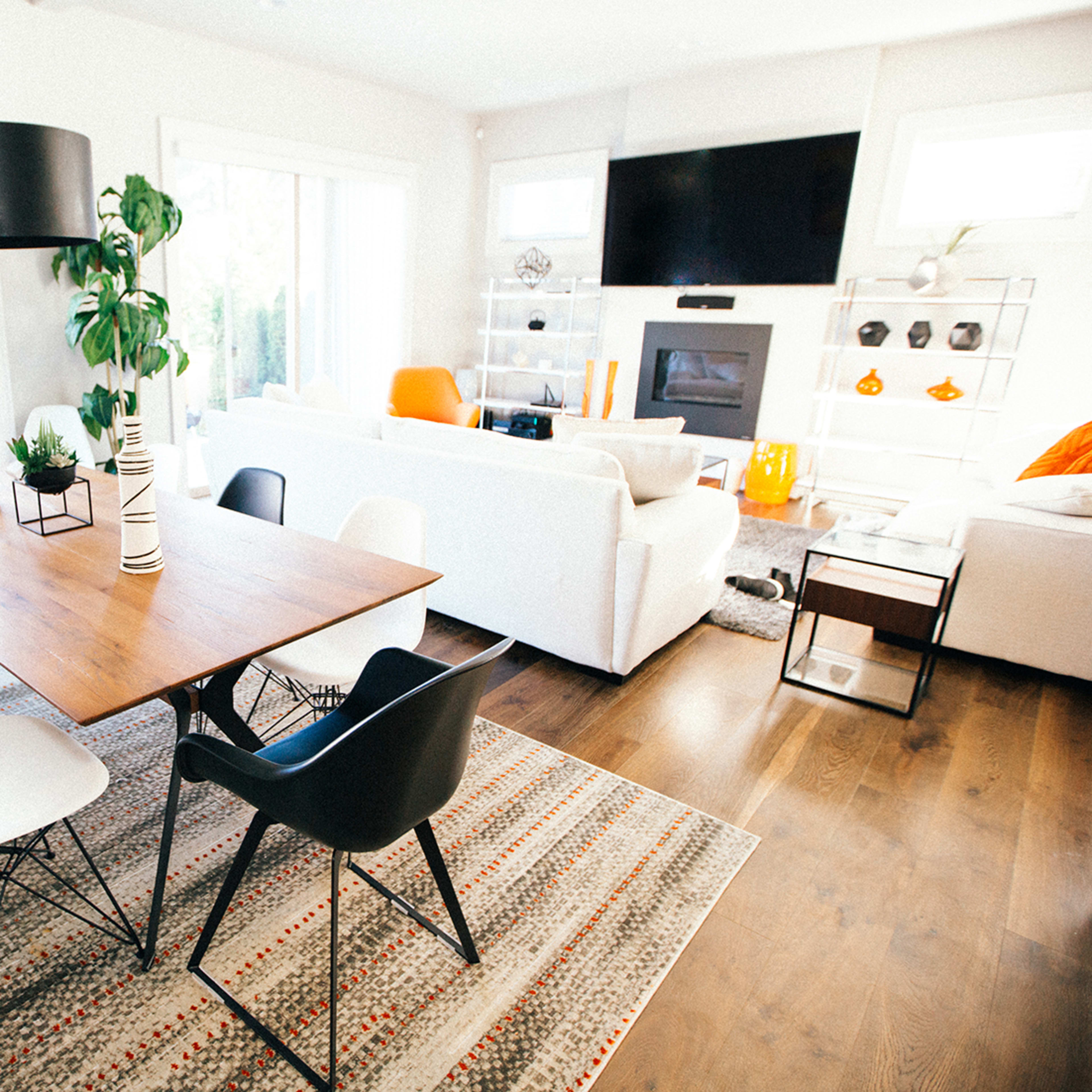 A dining area features a wooden table surrounded by black and white chairs, with large windows letting in natural light.
