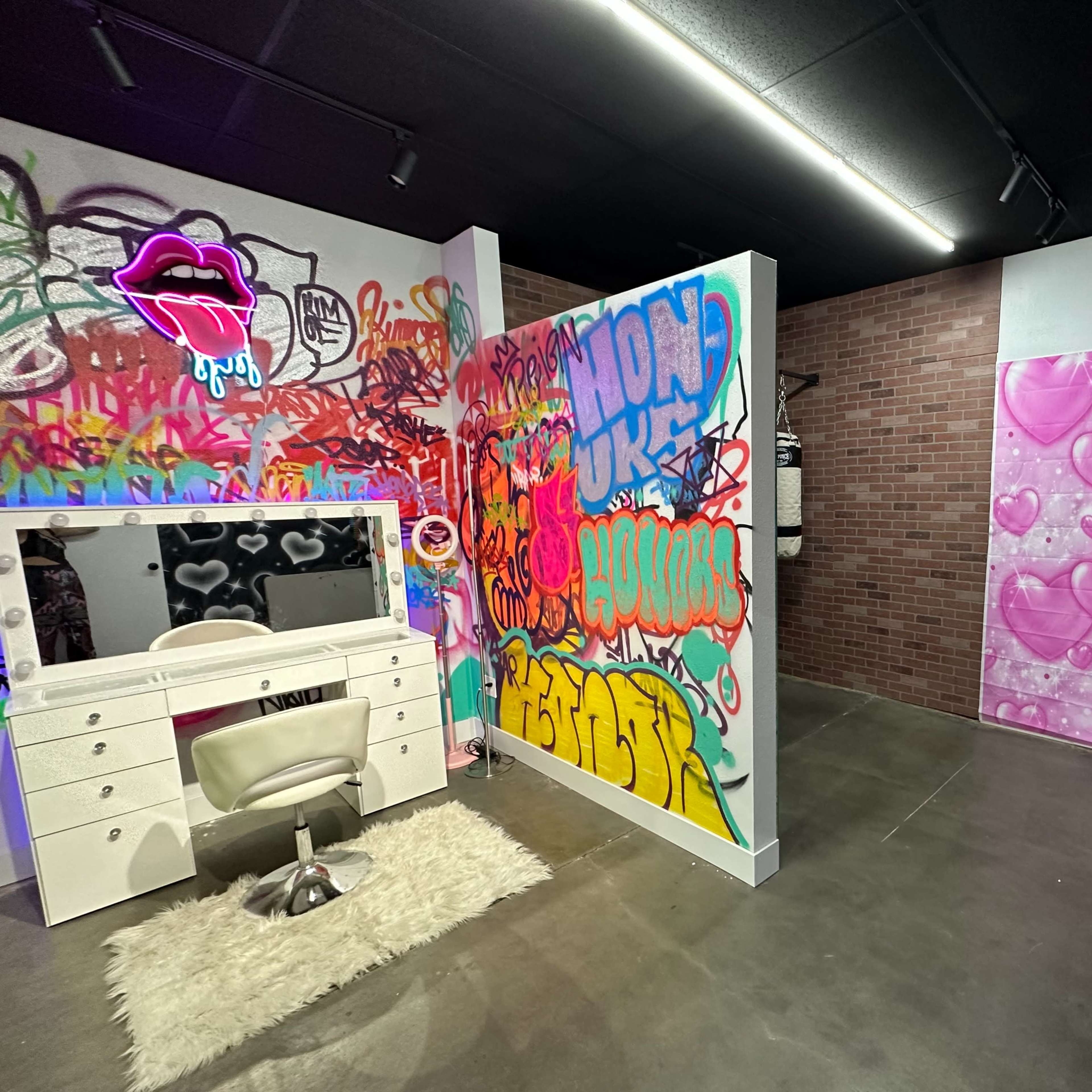 A decorative room featuring a white vanity with a chair, surrounded by colorful graffiti on the walls, including hearts and abstract designs.