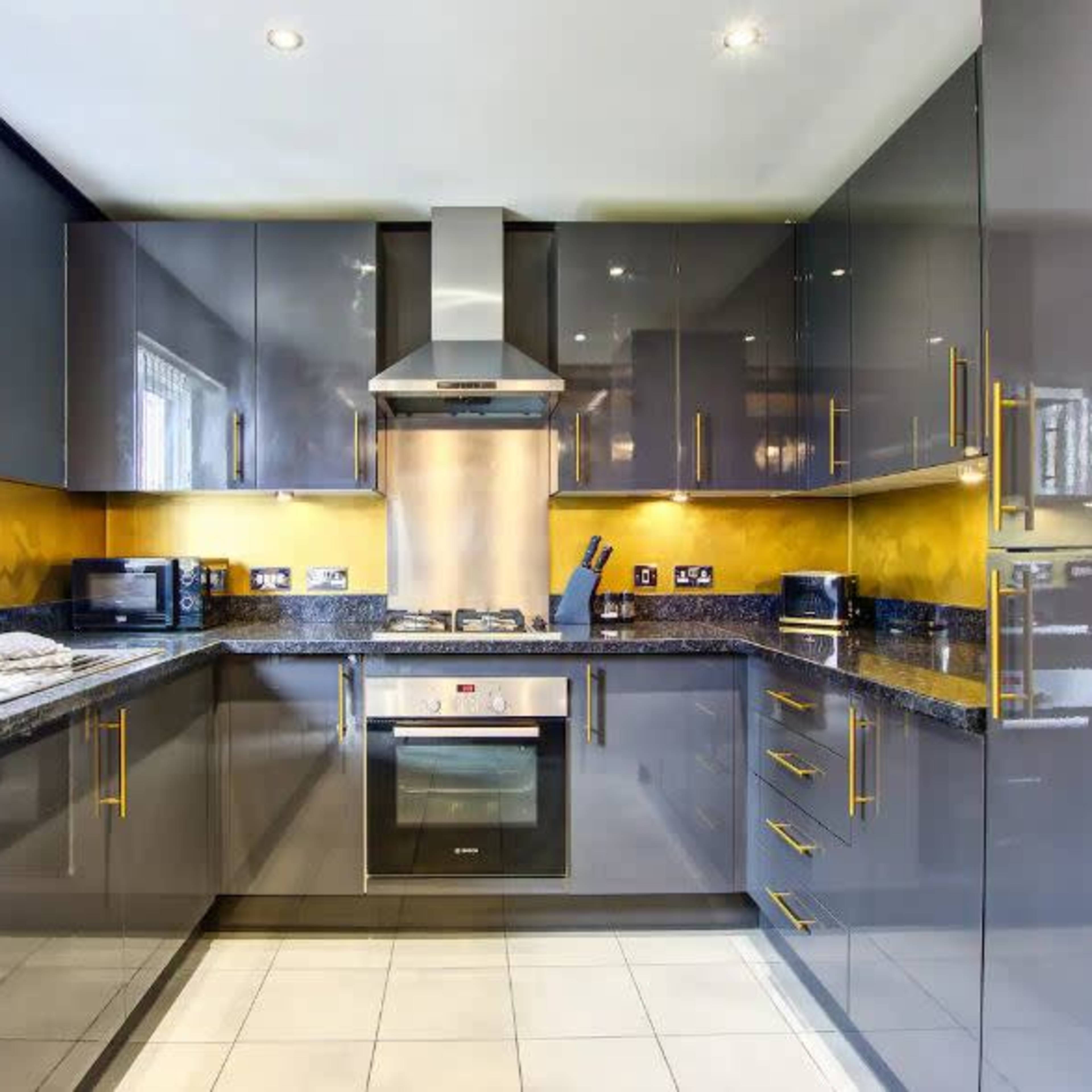 A modern kitchen featuring sleek gray cabinets, a stainless steel oven, and a yellow accent wall.