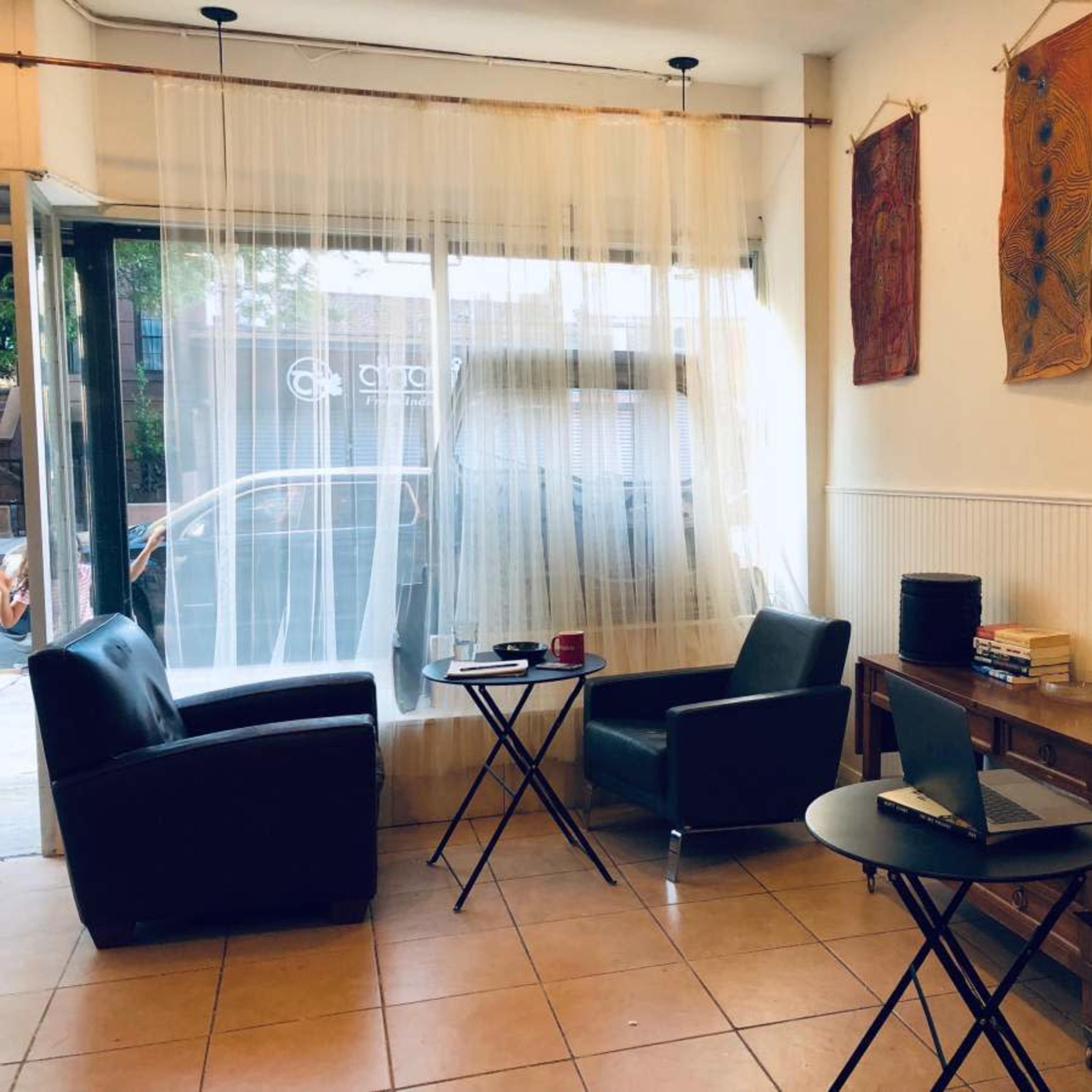 A small cafe interior with two black chairs, a round table, a laptop on a wooden side table, and artwork hanging on the walls.