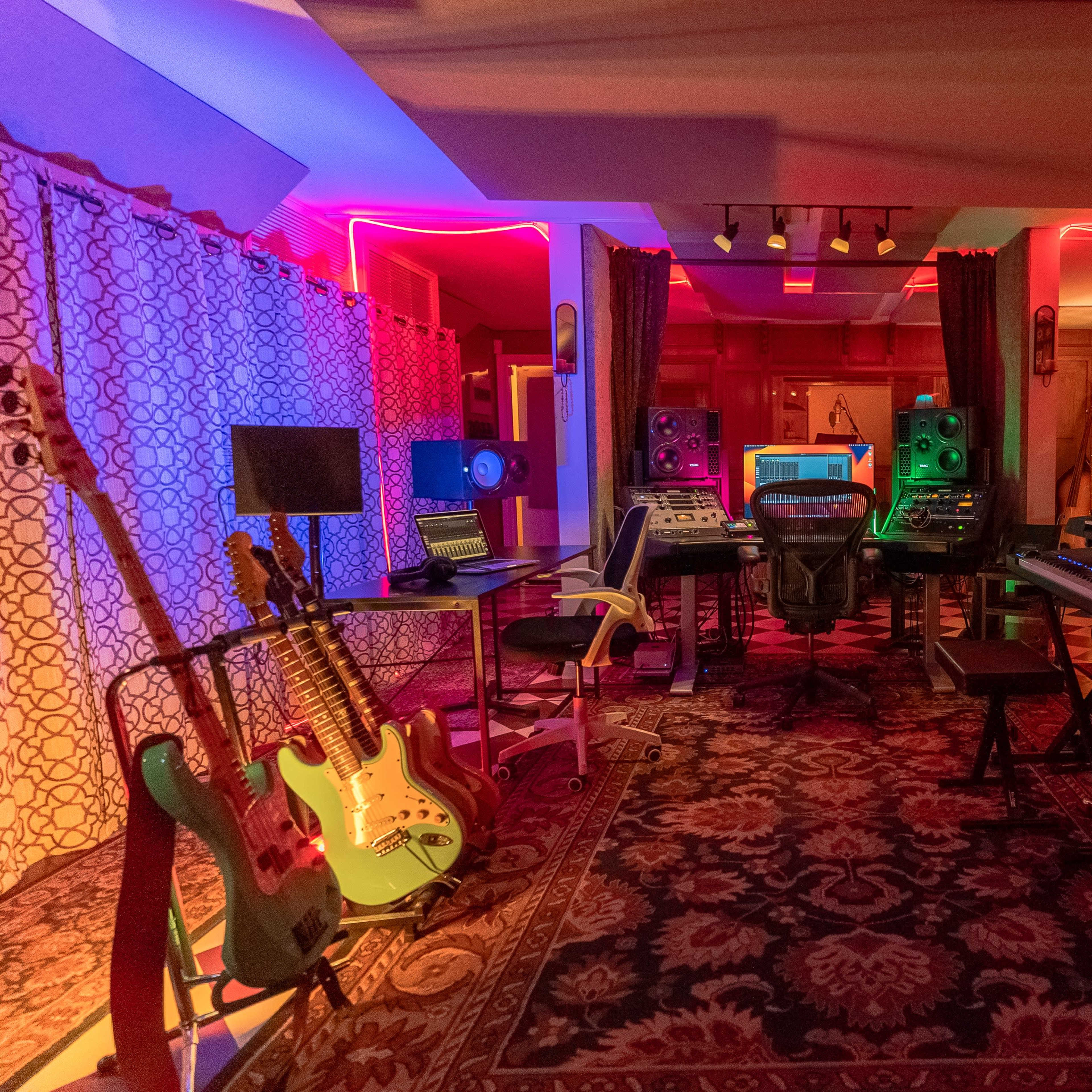 A music production studio with colorful ambient lighting, equipped with various musical instruments, mixing consoles, and sound equipment arranged around the room.