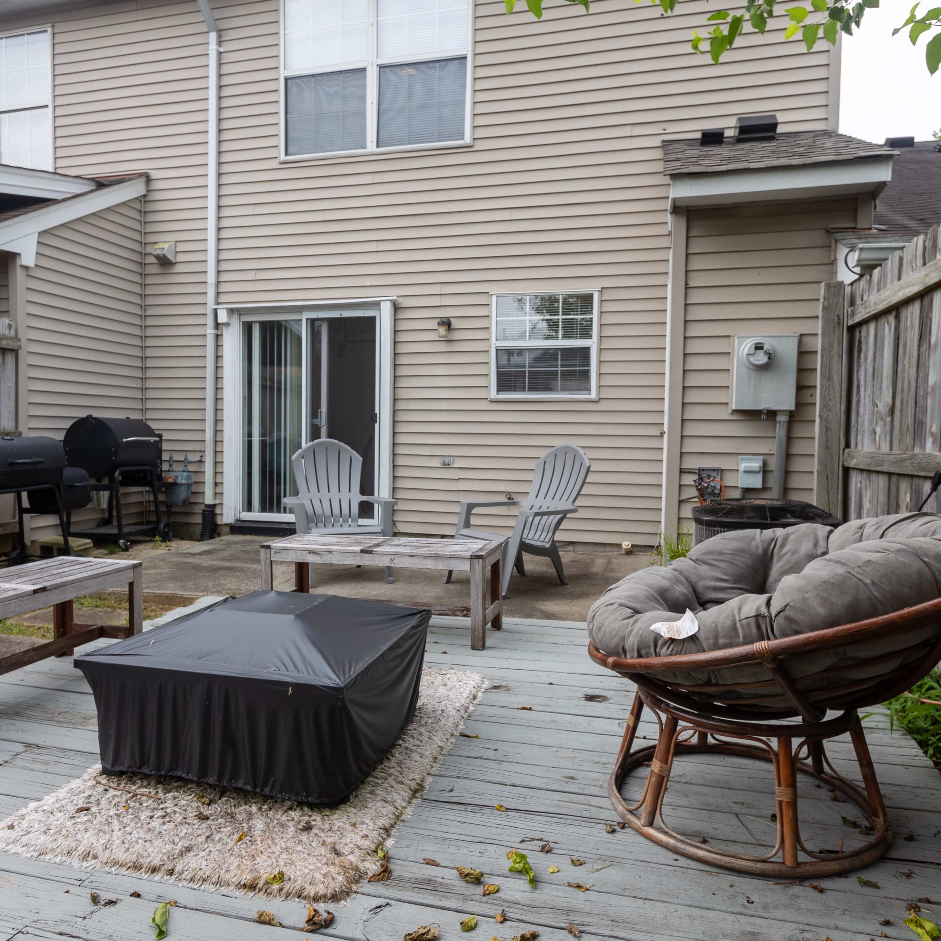 A backyard patio with wooden decking, featuring a circular chair, a small table, and a grill in the background.