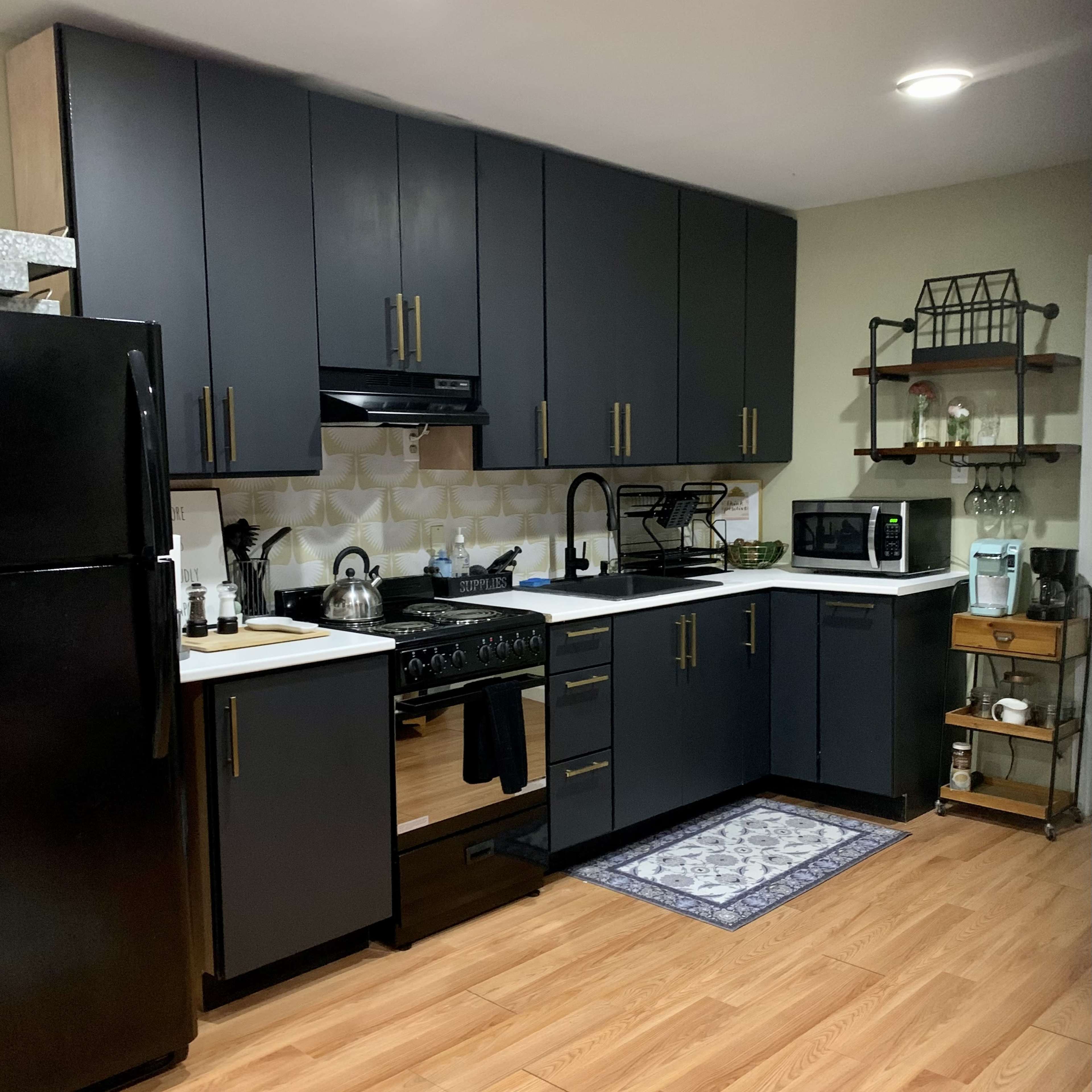 The kitchen features dark cabinetry, a black refrigerator, a gas stove, and a microwave, with a wooden floor and a patterned rug.