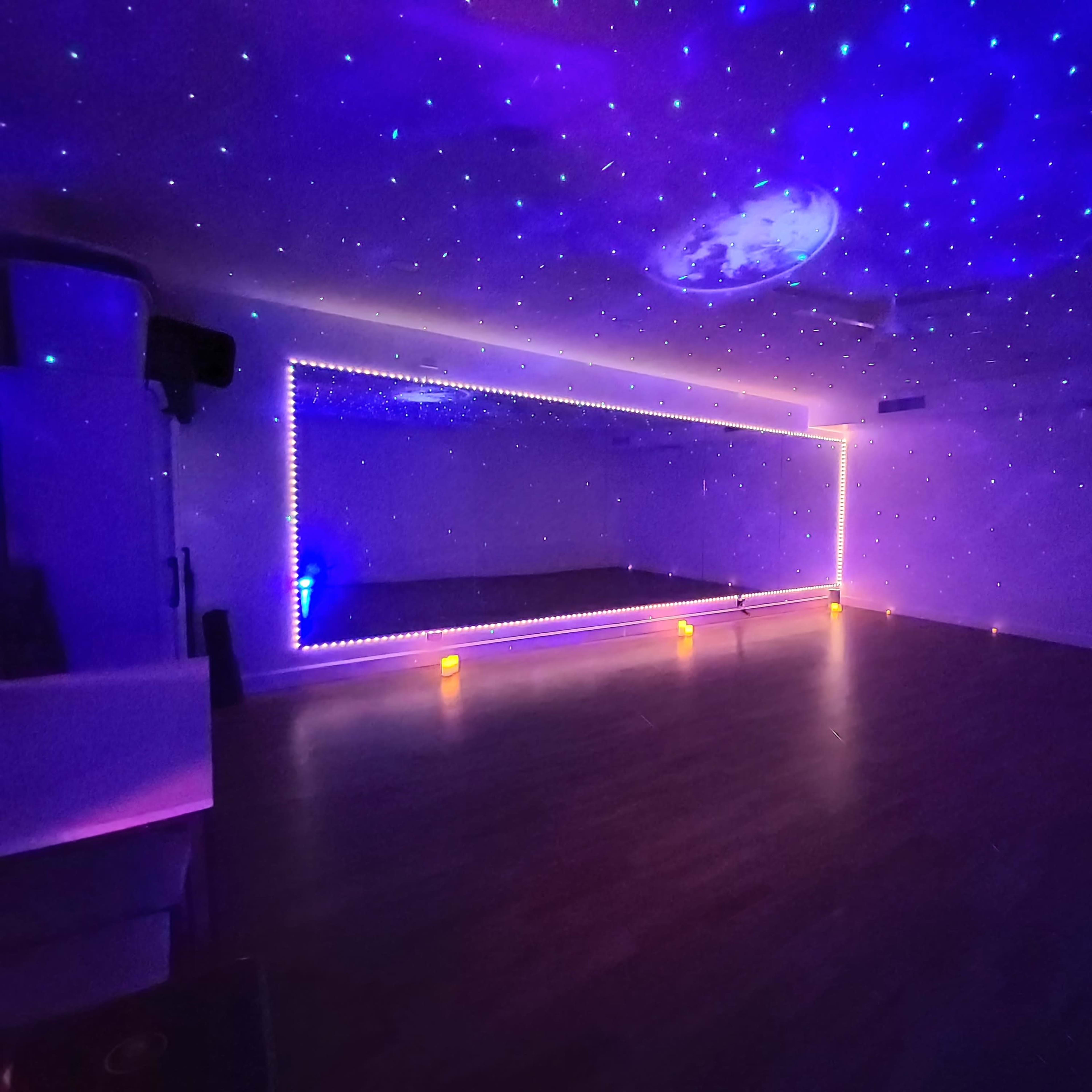A spacious room features a large mirror along one wall and a ceiling decorated with a starry projection, illuminated by soft lights.