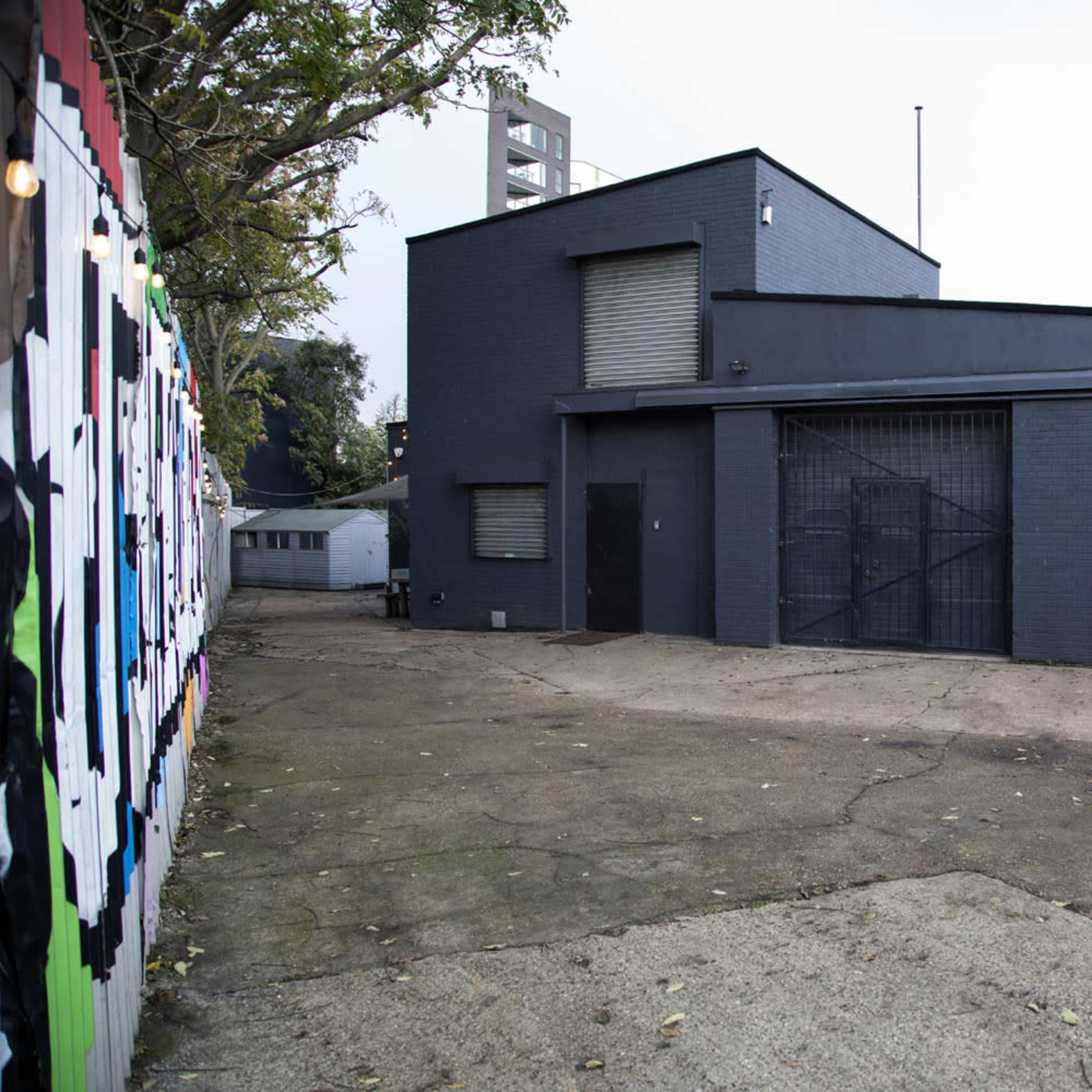 A dark gray building with barred windows, located beside a paved area and surrounded by a fence.
