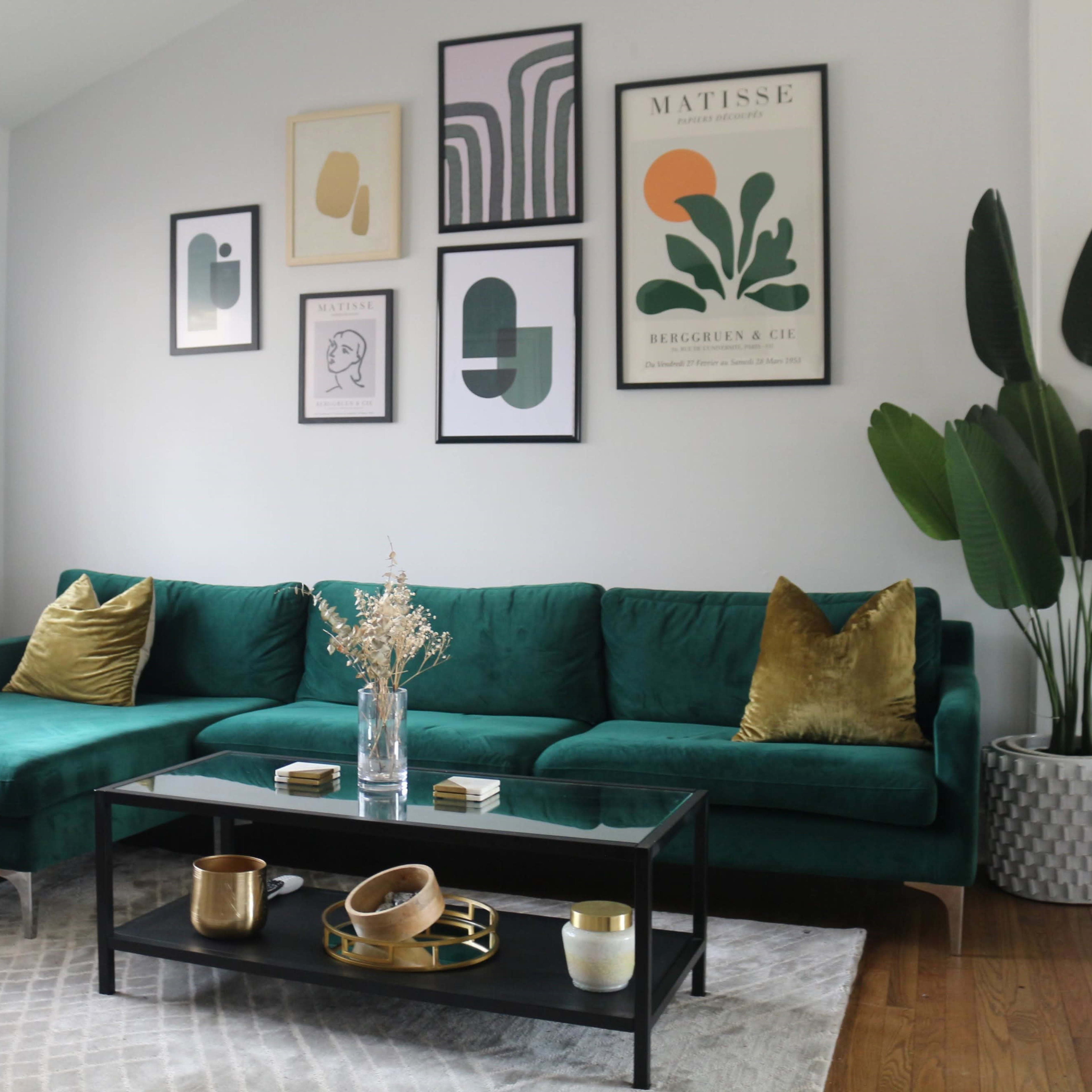 A modern living room featuring a green velvet sectional sofa, a black coffee table with decorative items, and framed art on the walls.