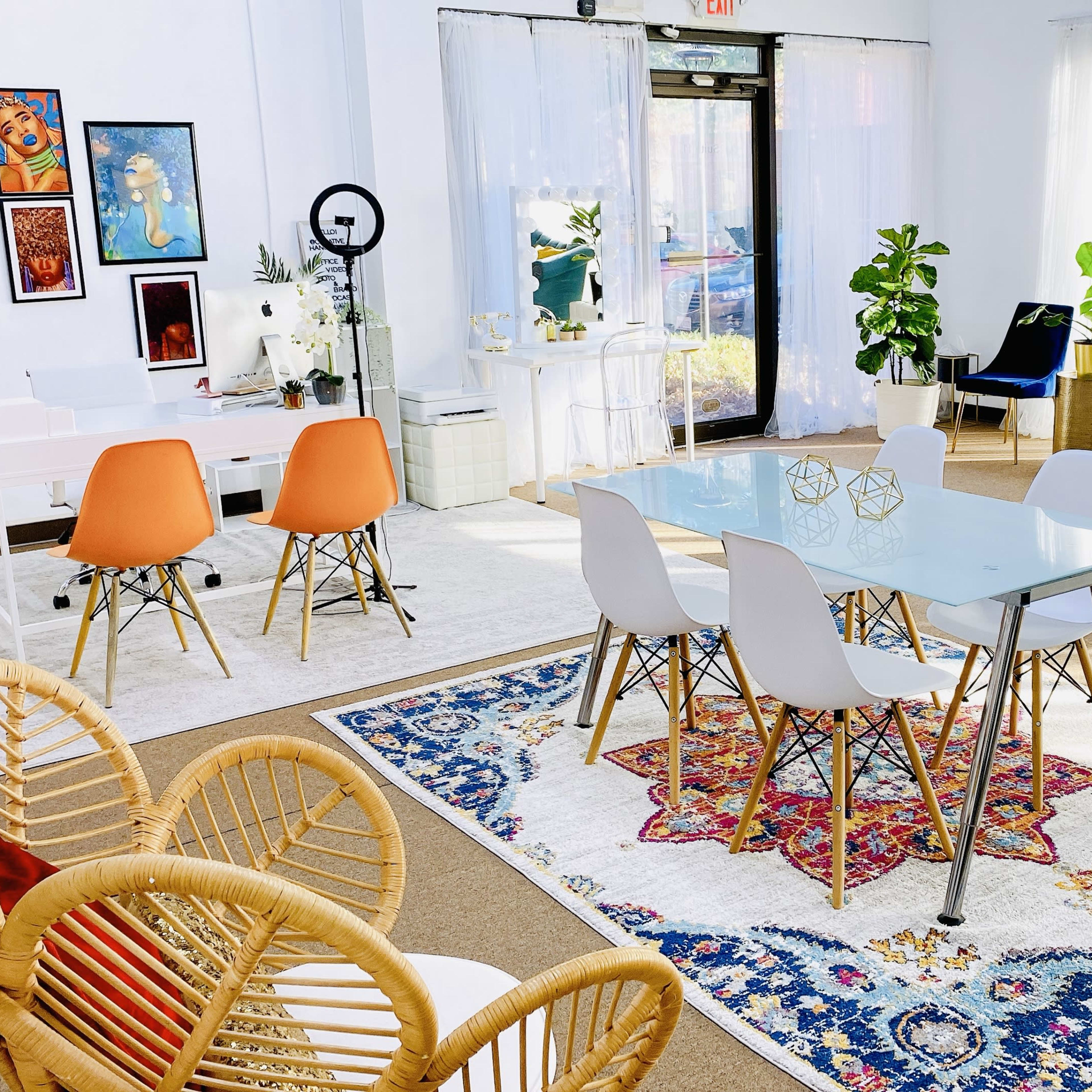 A brightly lit, modern interior featuring a dining table with white chairs, a blue sofa, various plants, and colorful artwork on the walls.