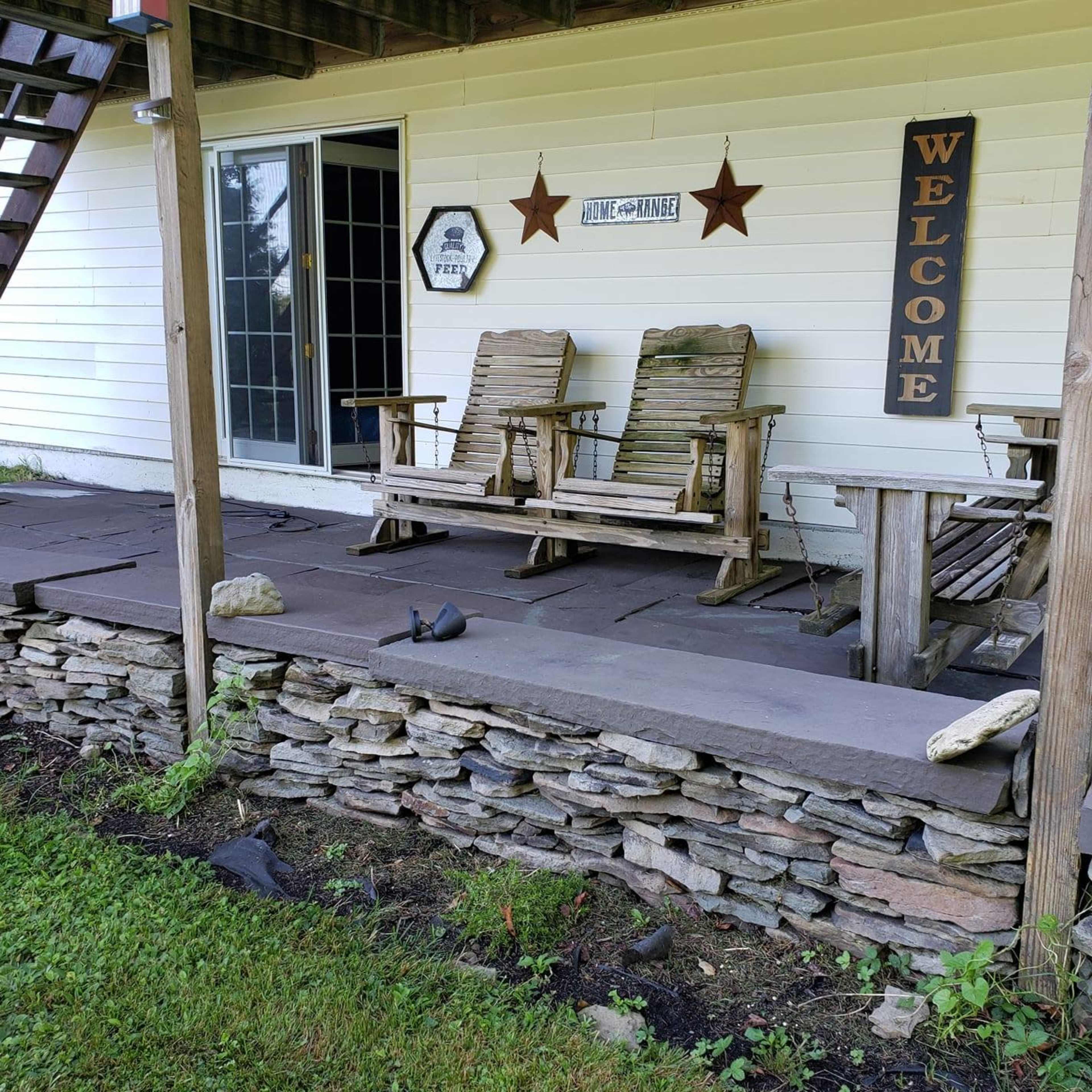 A porch area with two wooden rocking chairs, a welcome sign, and a stone wall beneath it.