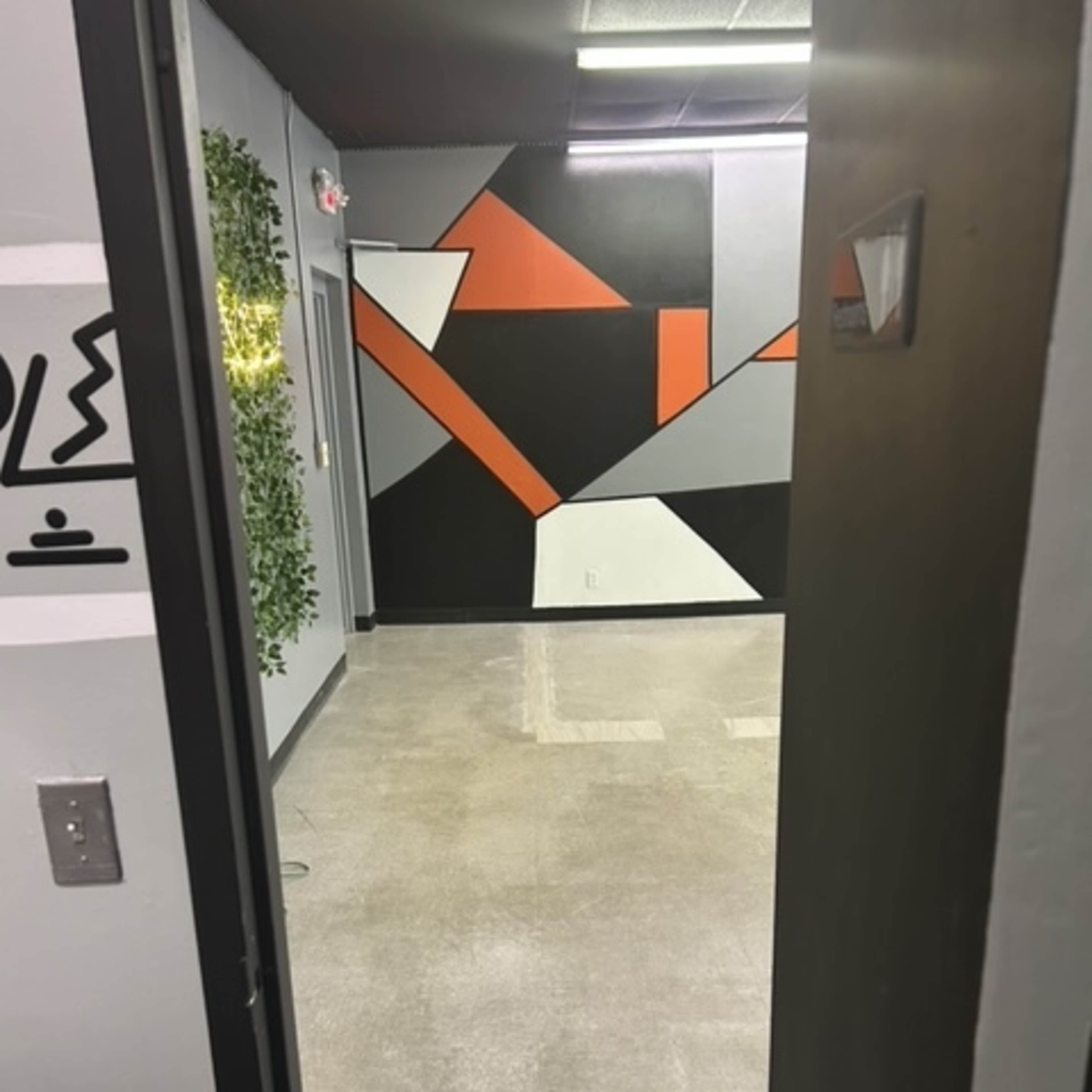 An open door leading into a room with a geometric wall mural and plain gray flooring.