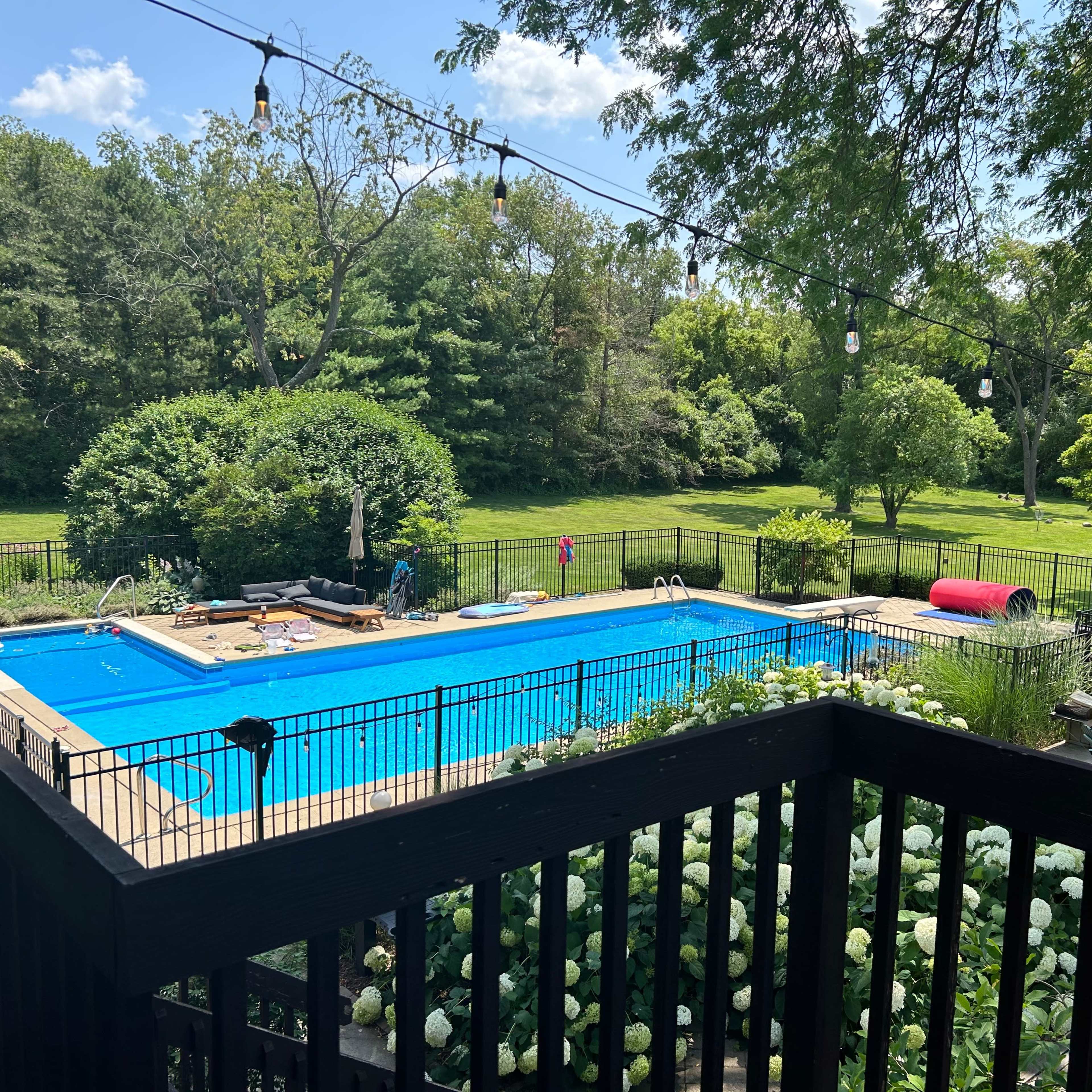 A rectangular swimming pool surrounded by a black fence and greenery is visible from an elevated deck.