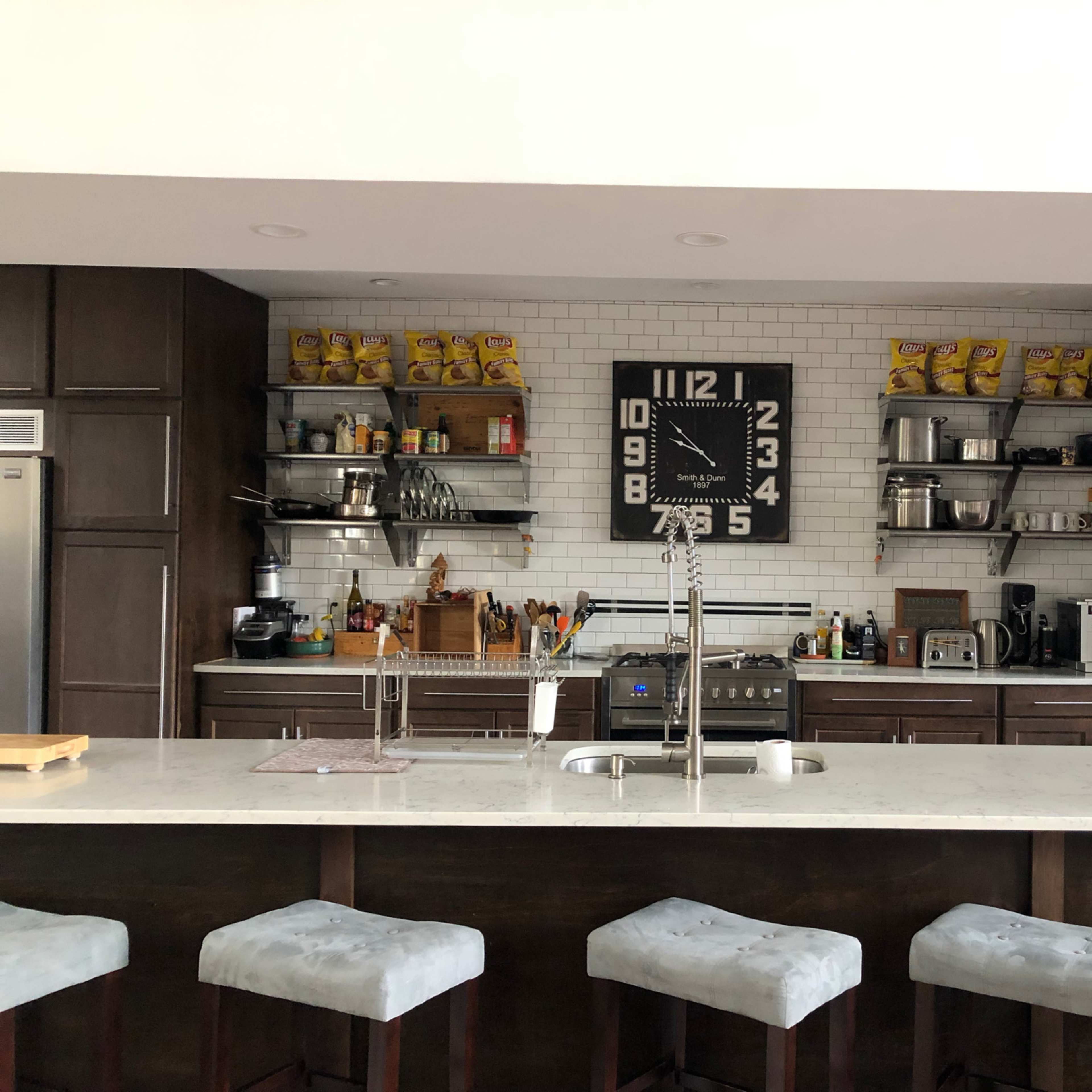 A modern kitchen with dark wood cabinetry, a large clock, and shelves displaying various kitchen items and appliances.