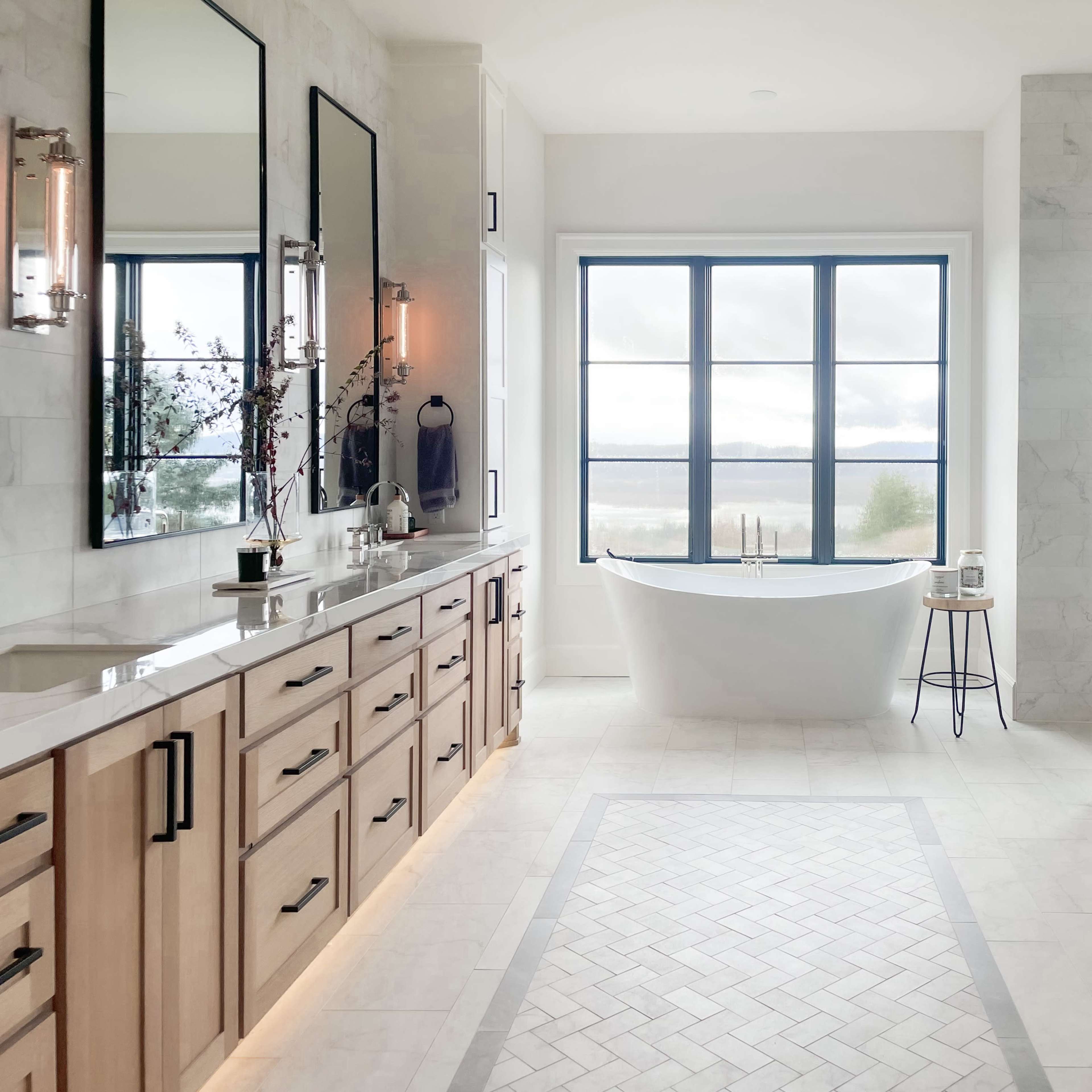 A spacious bathroom featuring a freestanding bathtub, double vanities with mirrors, and large windows providing a view of the outdoors.
