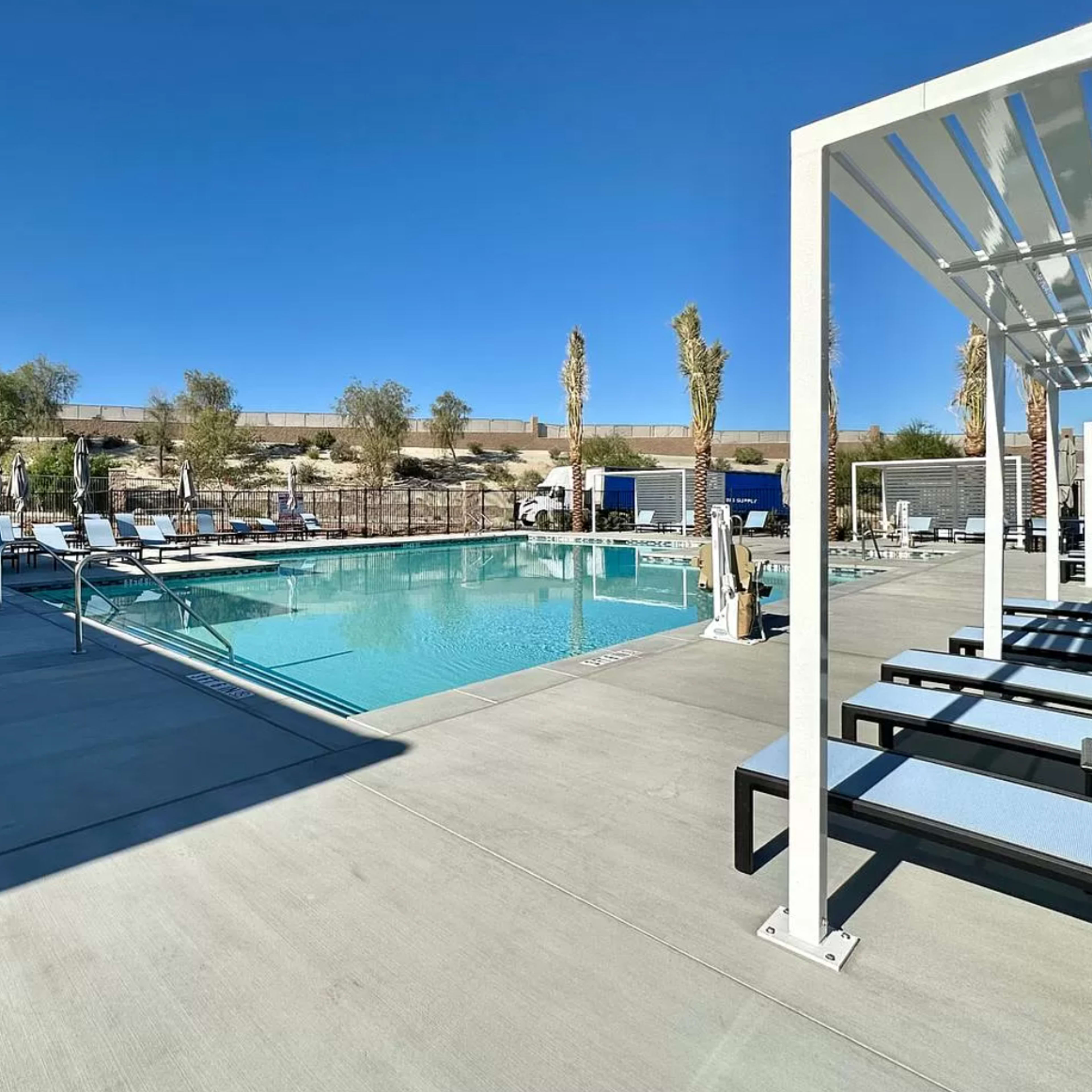 A clear blue pool is surrounded by lounge chairs and palm trees, with a desert landscape visible in the background.