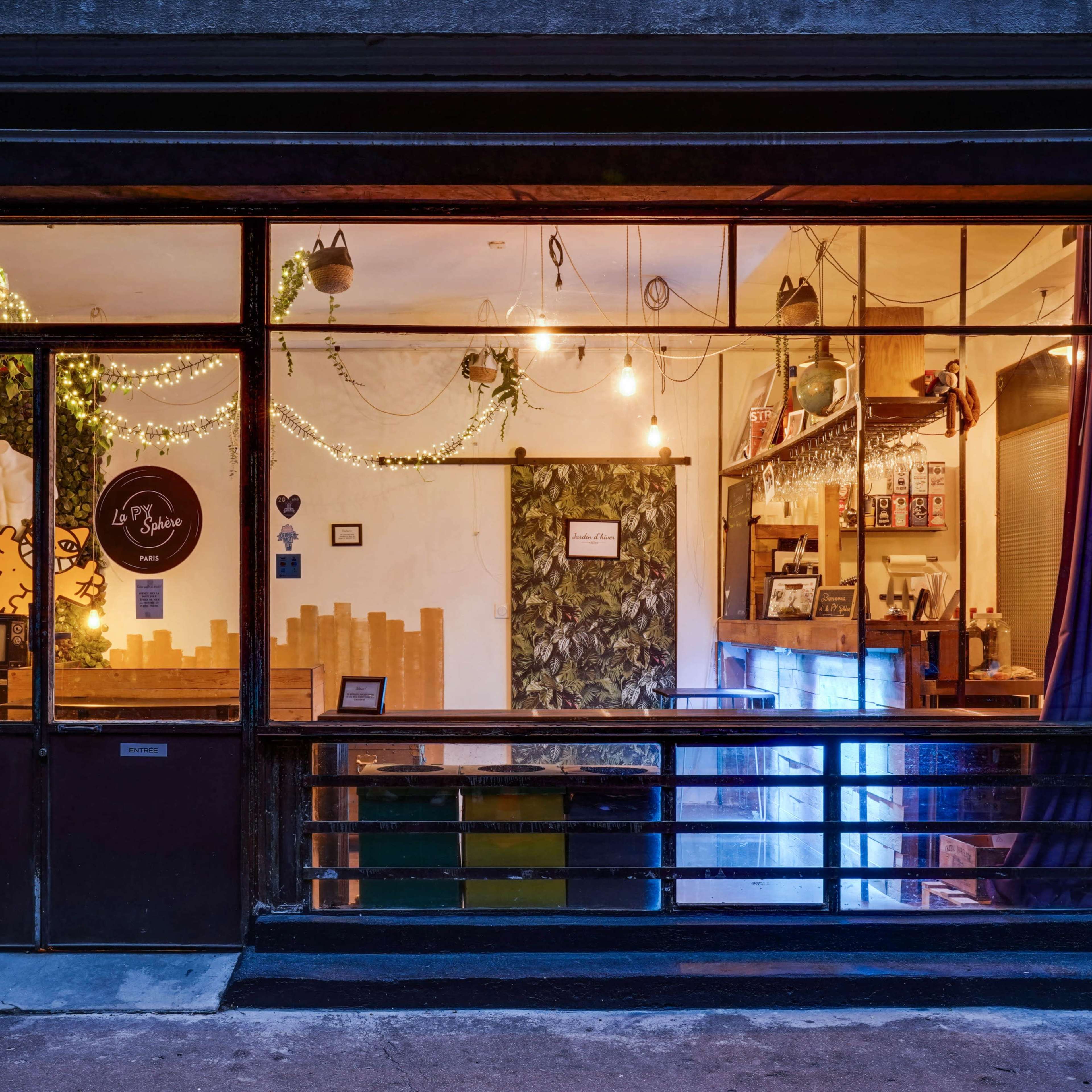 A shop window displays a cozy interior adorned with plants, lights, and wooden decor.