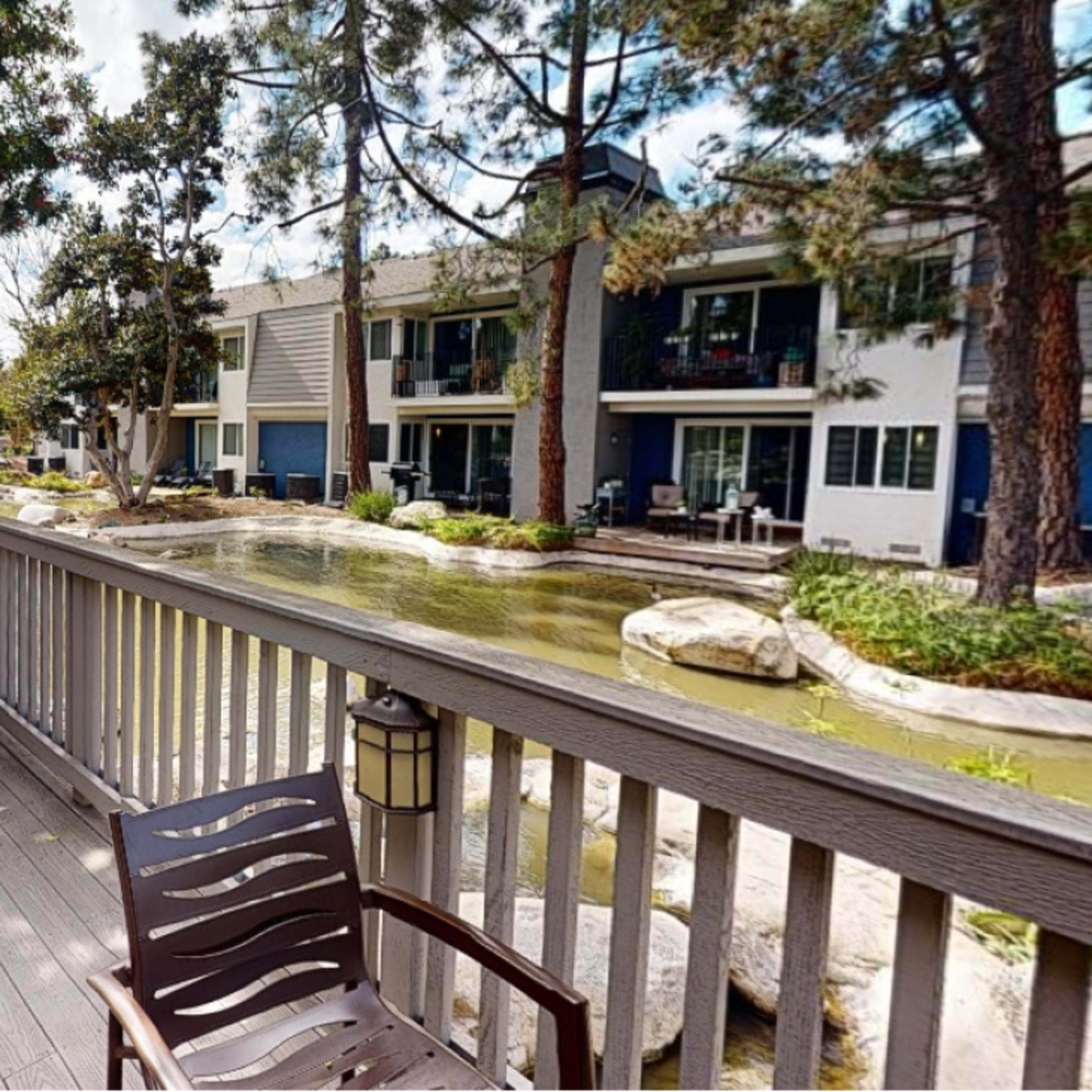 A deck with two chairs overlooks a pond surrounded by residential buildings and trees.
