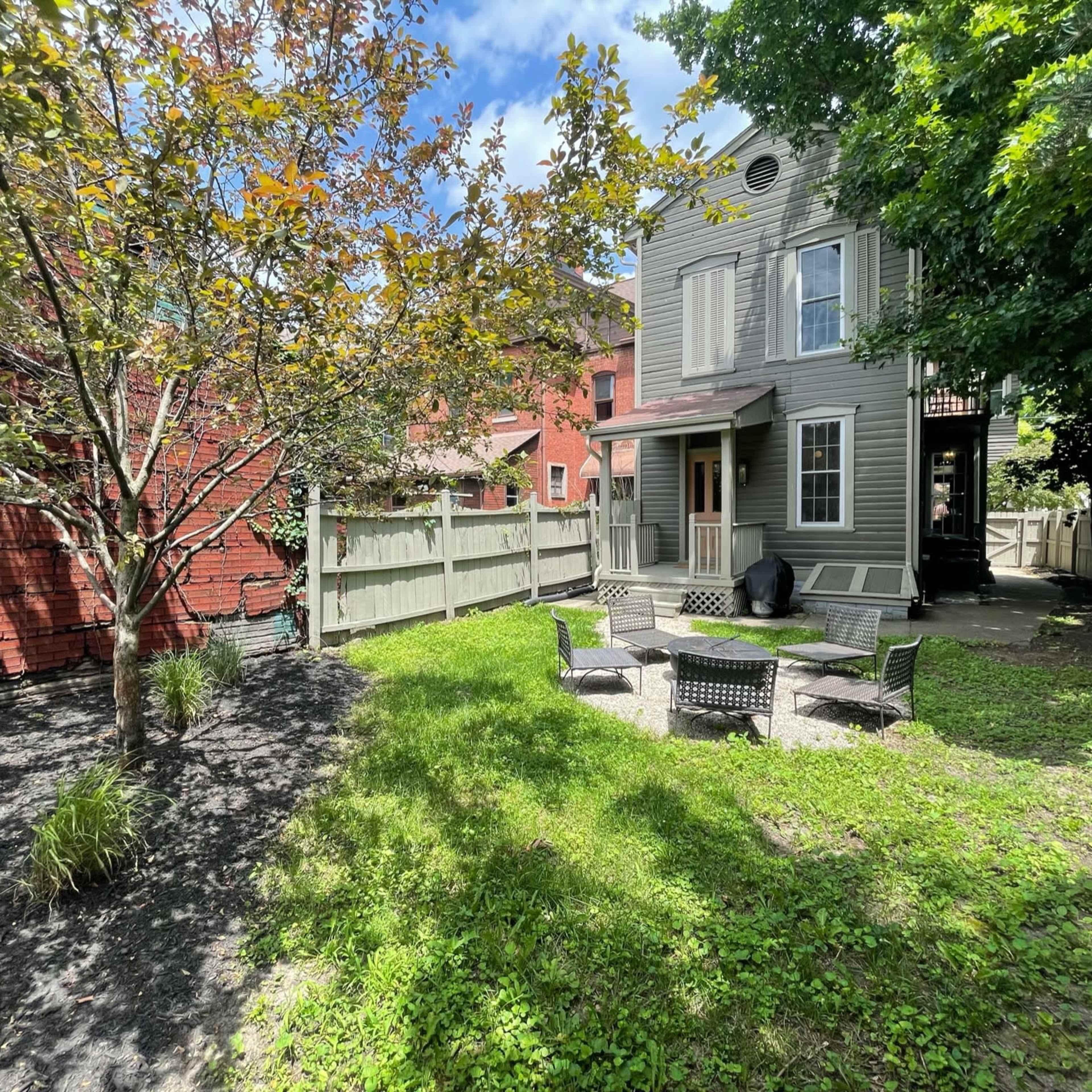 A backyard with a well-maintained lawn, a small seating area, and a tree, enclosed by wooden fencing.