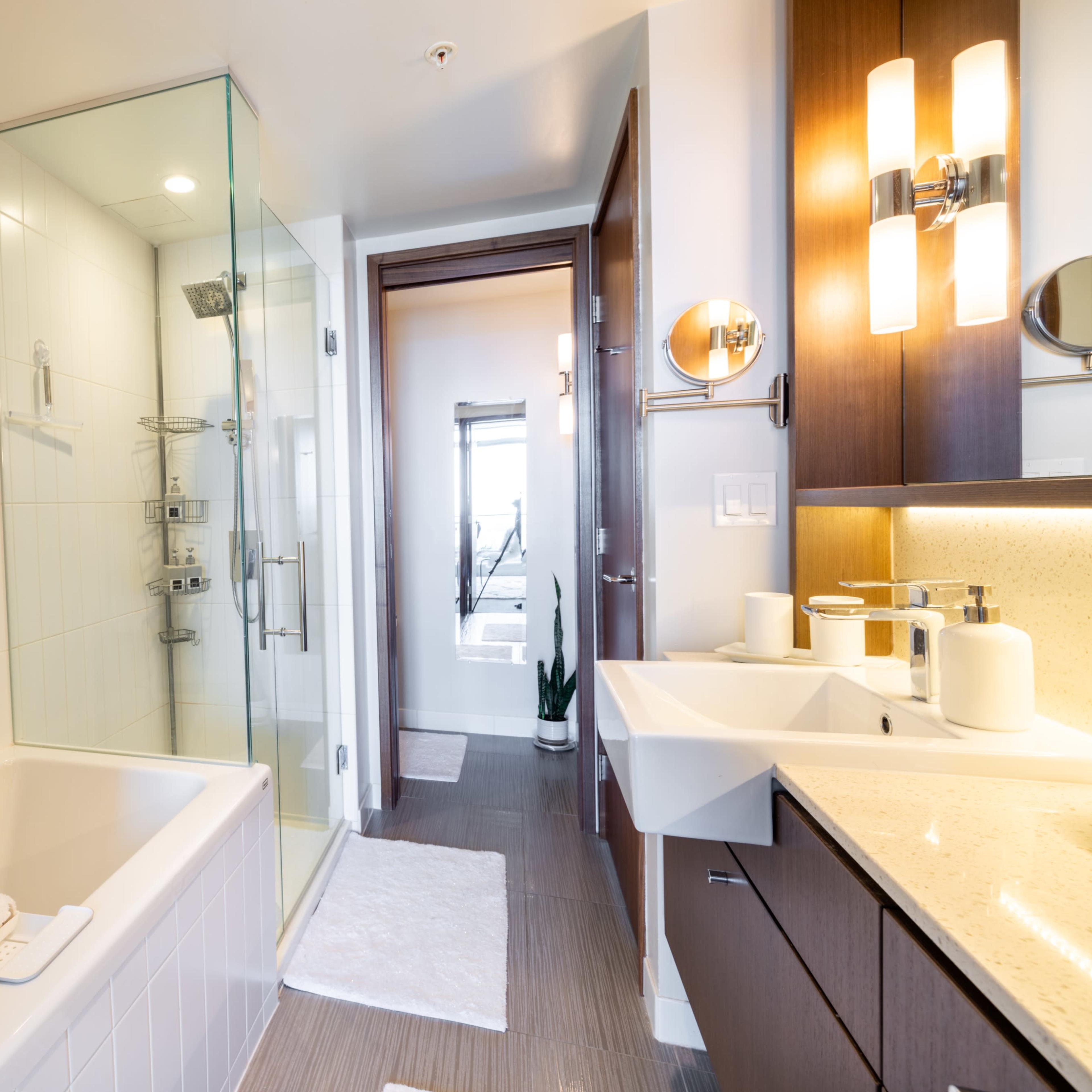 A modern bathroom with a glass shower enclosure, a bathtub, and a wooden vanity with a sink and mirror.