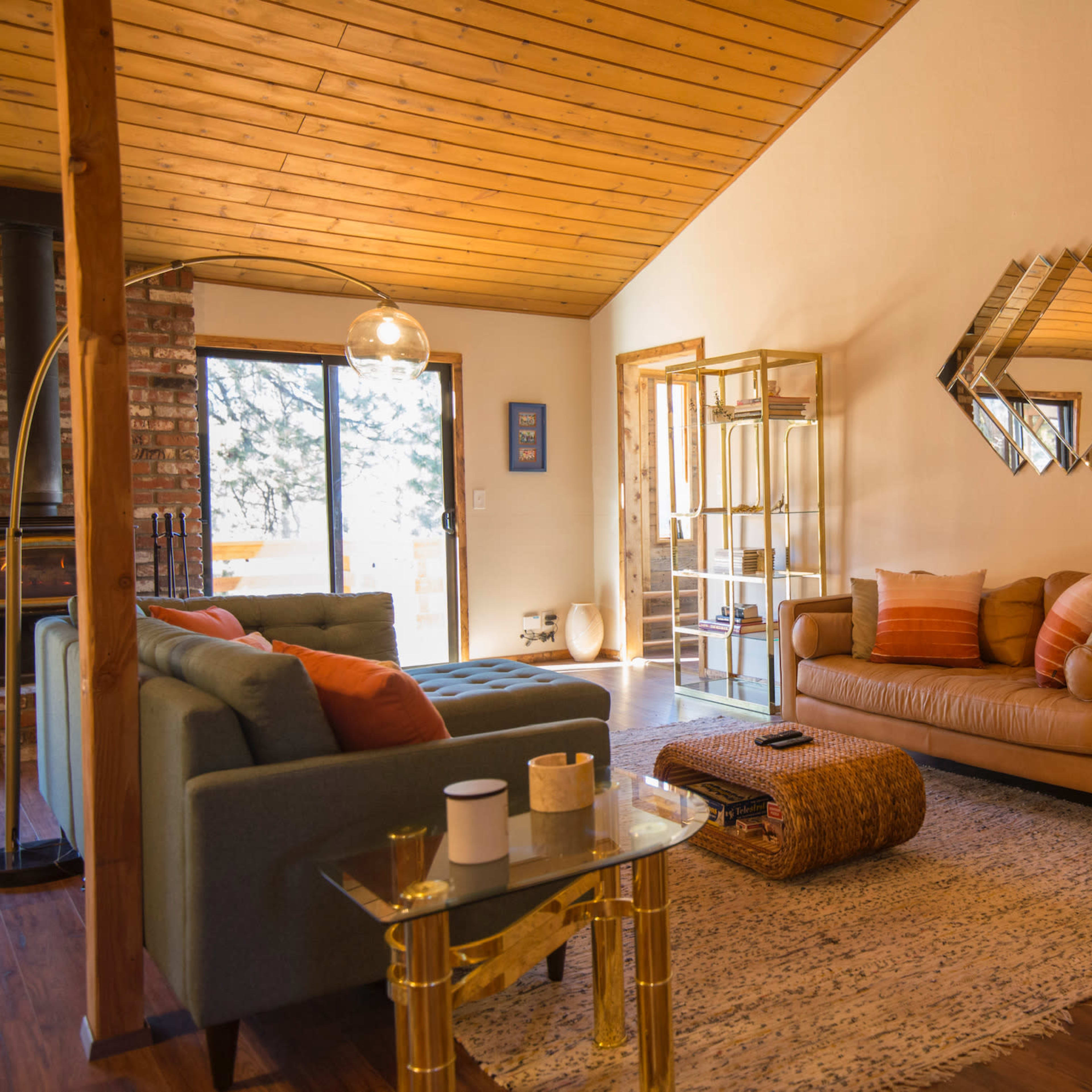 A cozy living room with two sofas, a coffee table, and a decorative mirror on the wall, surrounded by large windows that let in natural light.