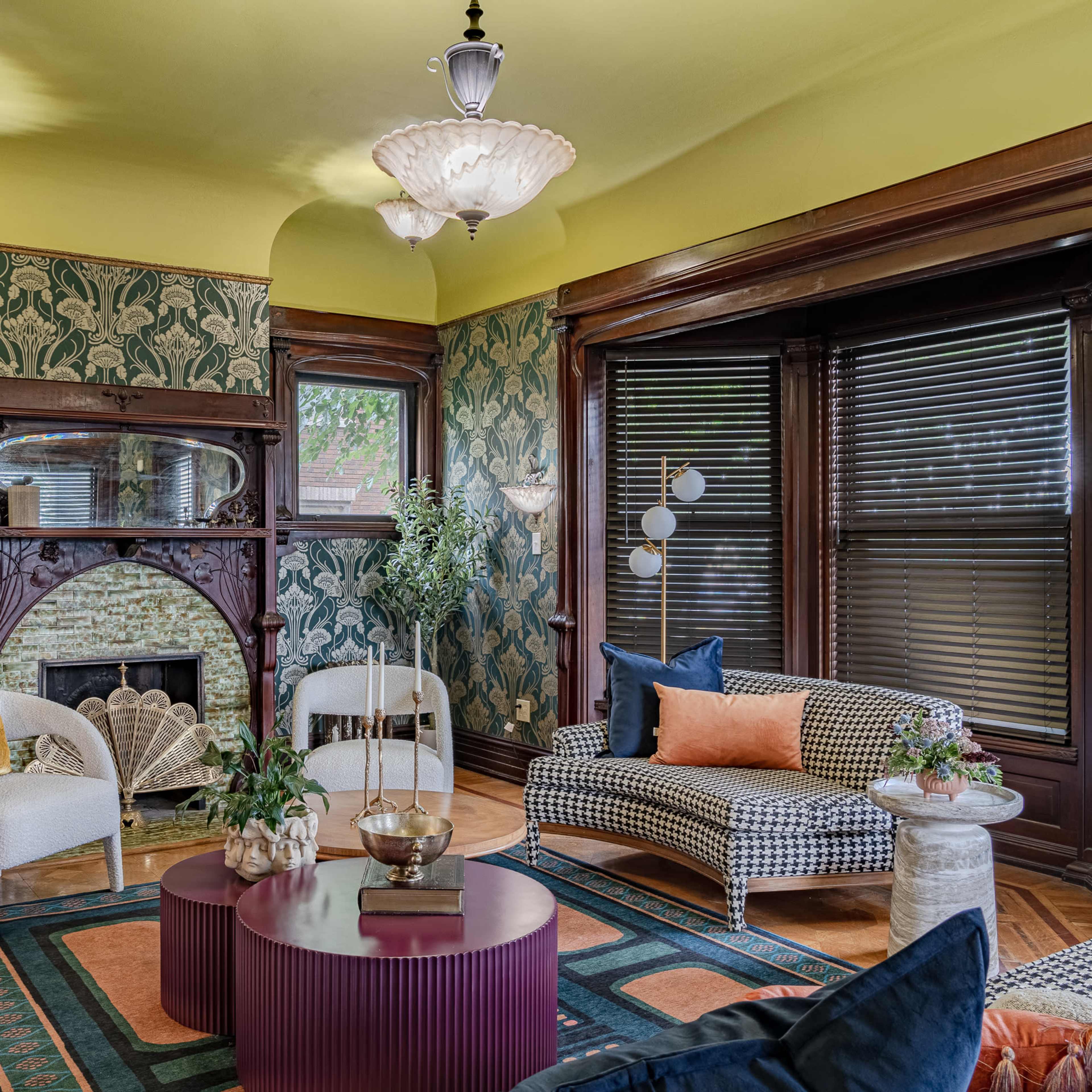 A vintage-style living room with patterned wallpaper, a decorative fireplace, and a mix of modern and classic furniture.