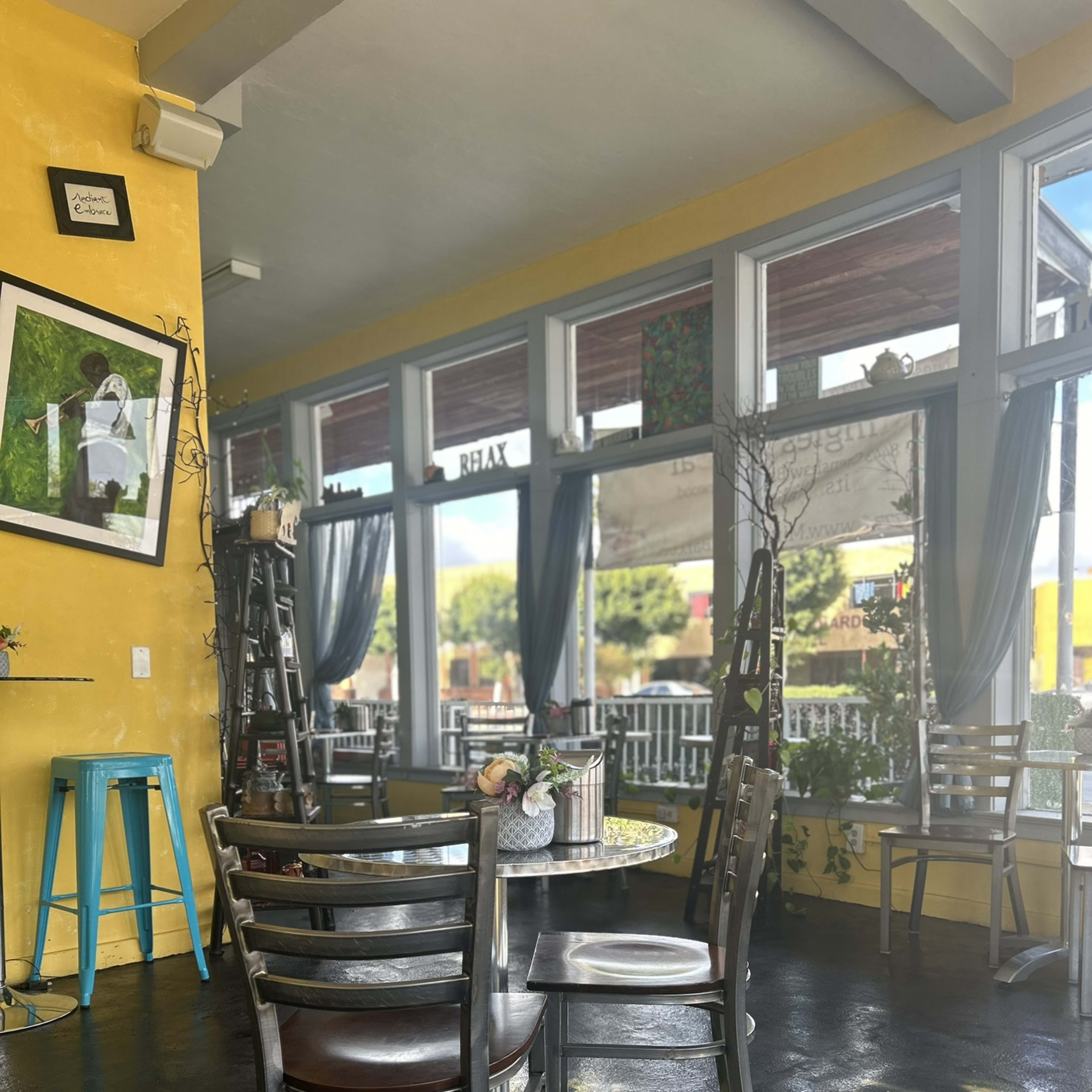 A brightly colored café interior with yellow walls, large windows, and tables arranged near the windows.