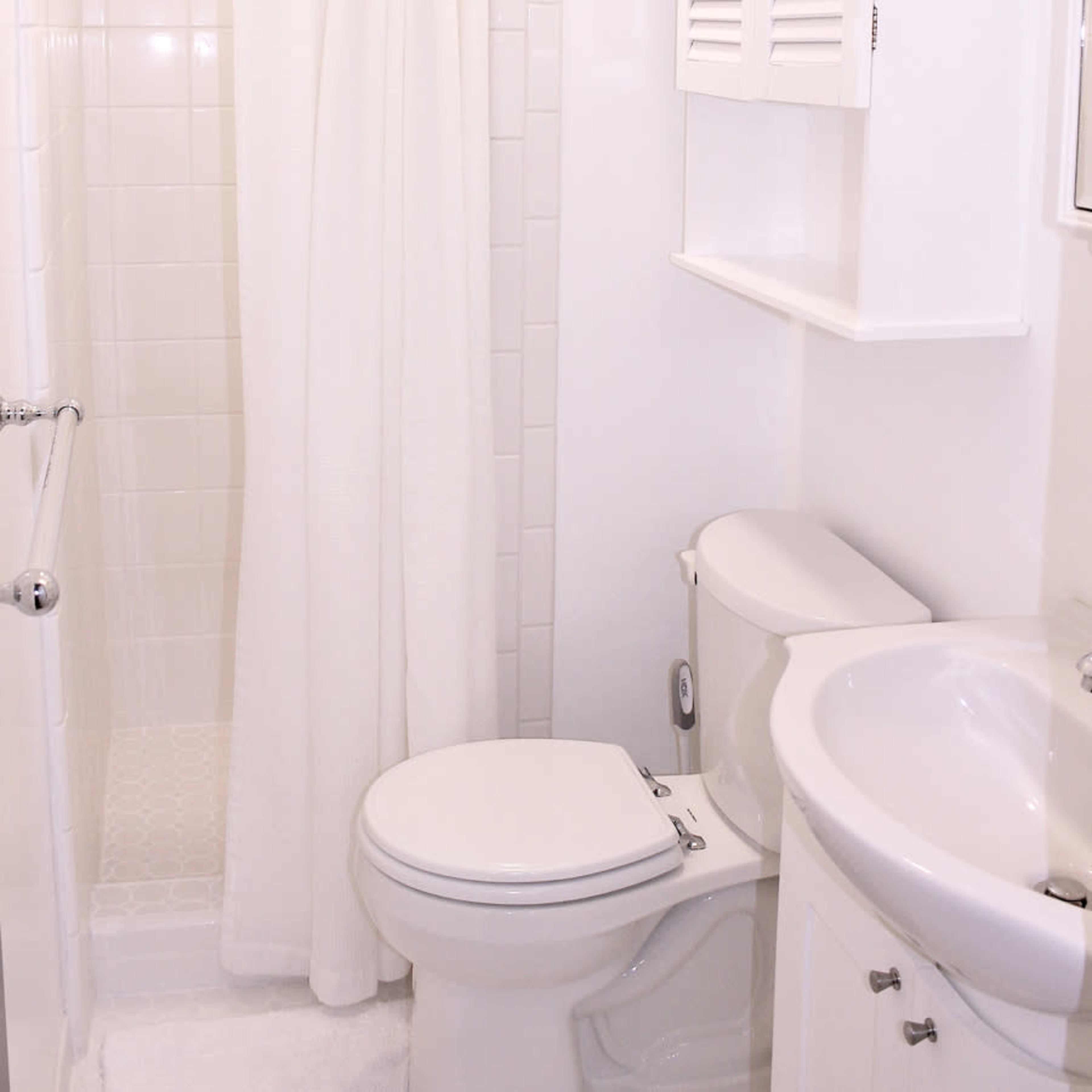A small bathroom featuring a shower with a white curtain, a toilet, and a sink with a cabinet above it.