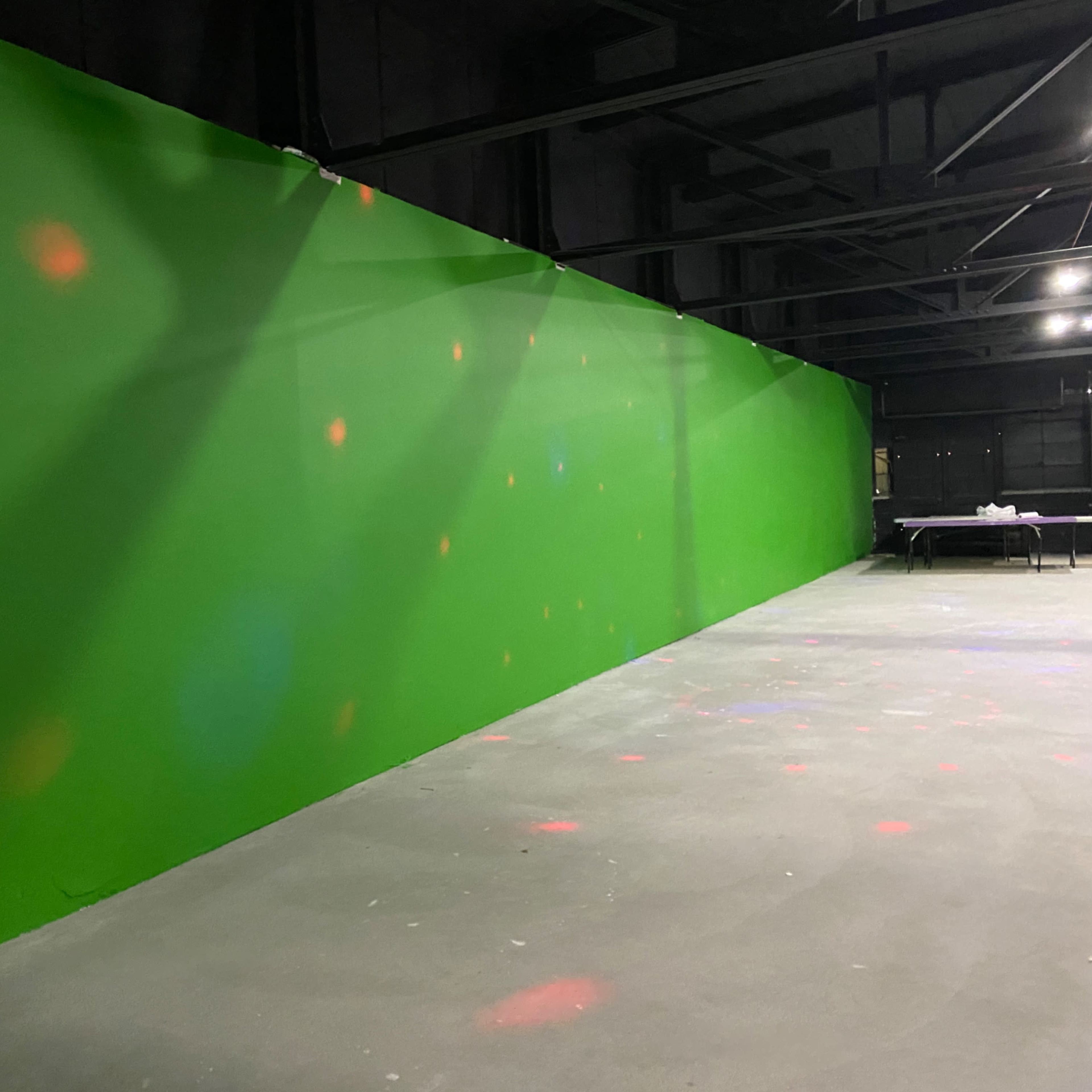 A large green wall in an industrial space with scattered colored lights on the floor.